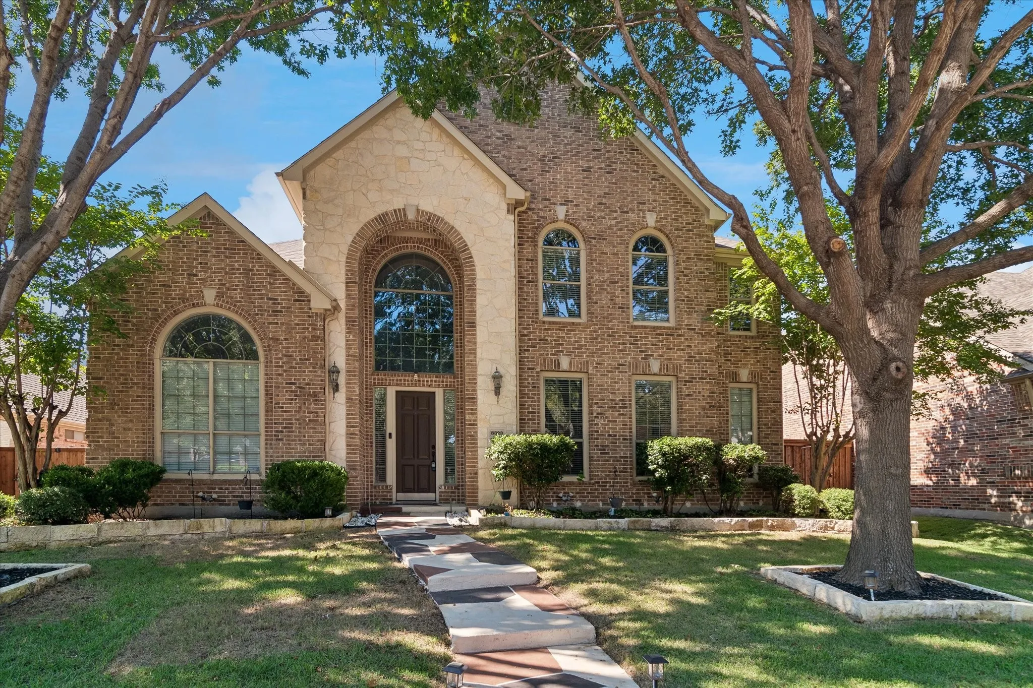 Brick and stone facade featuring arched windows, a prominent arched entry, and a patterned walkway