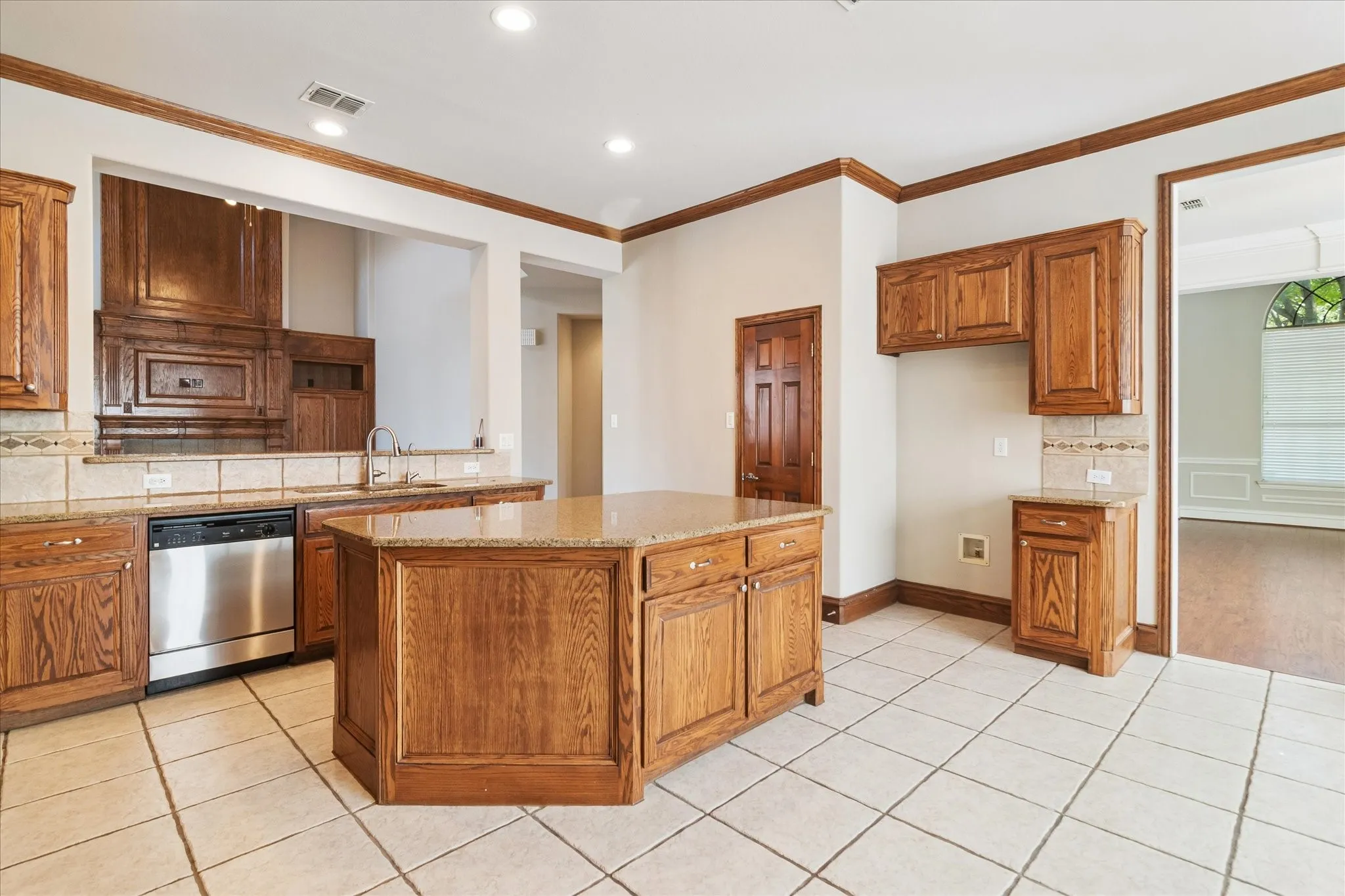 Kitchen featuring an island with wood-finish cabinetry, tile flooring, built-in stainless steel dishwasher, and stone countertops