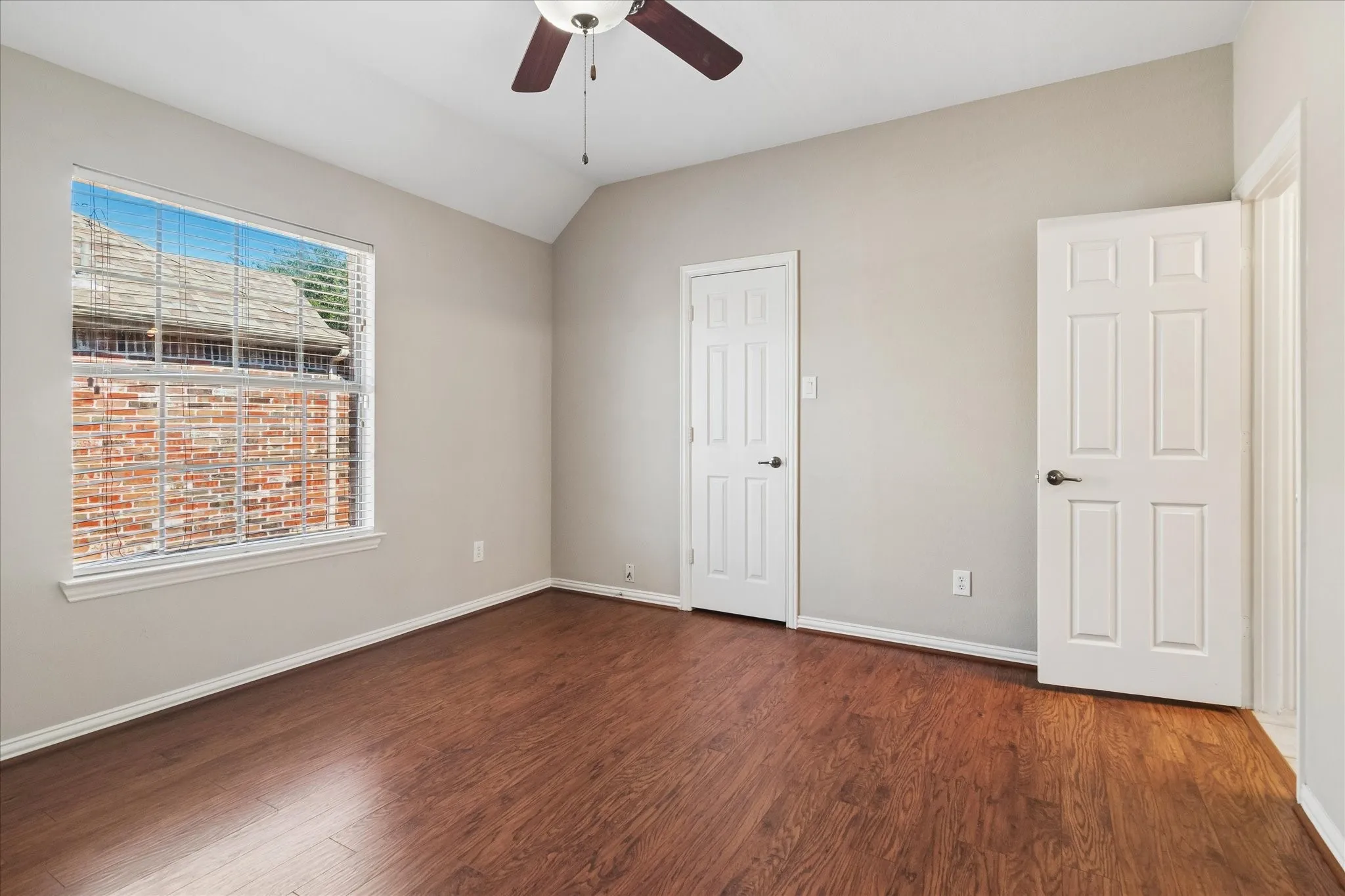 Vaulted ceiling with a ceiling fan, wood-finish flooring, and a large window with horizontal blinds