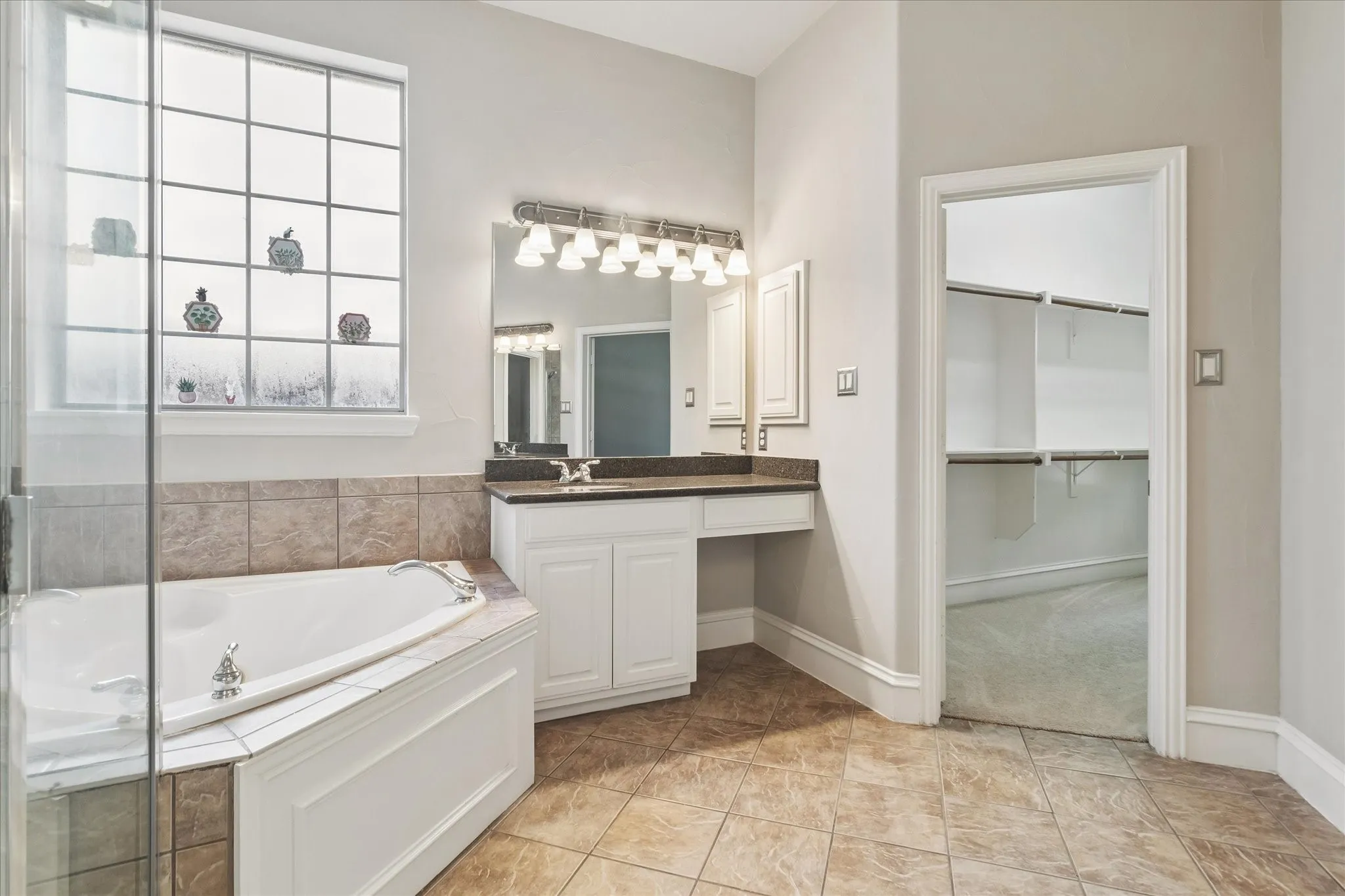 Corner soaking tub with tiled surround, adjacent glass-enclosed shower, dual vanity with undermount sinks, and separate water closet