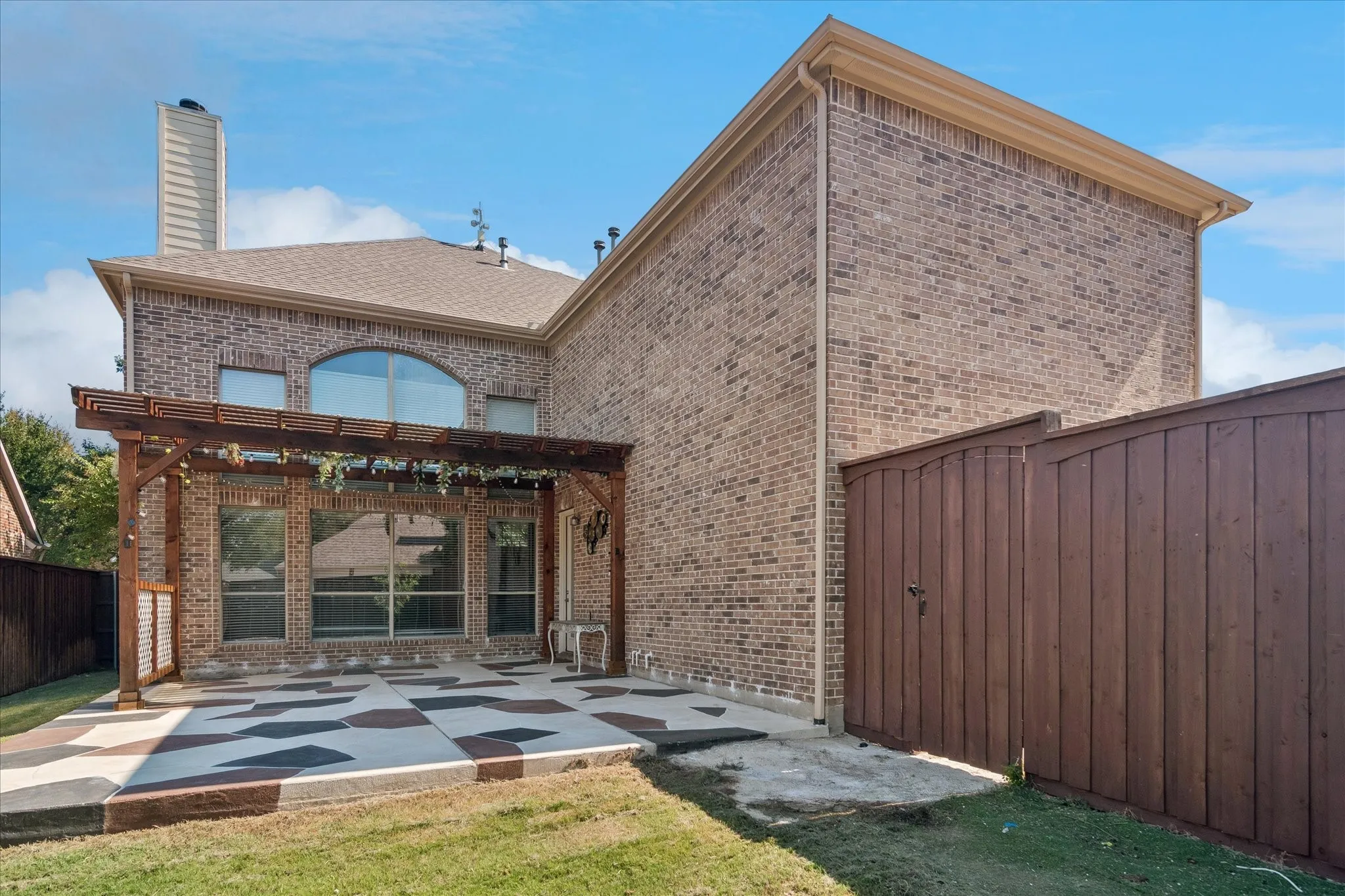 Brick exterior with a wood pergola, patterned concrete patio, full privacy fence, and large window openings