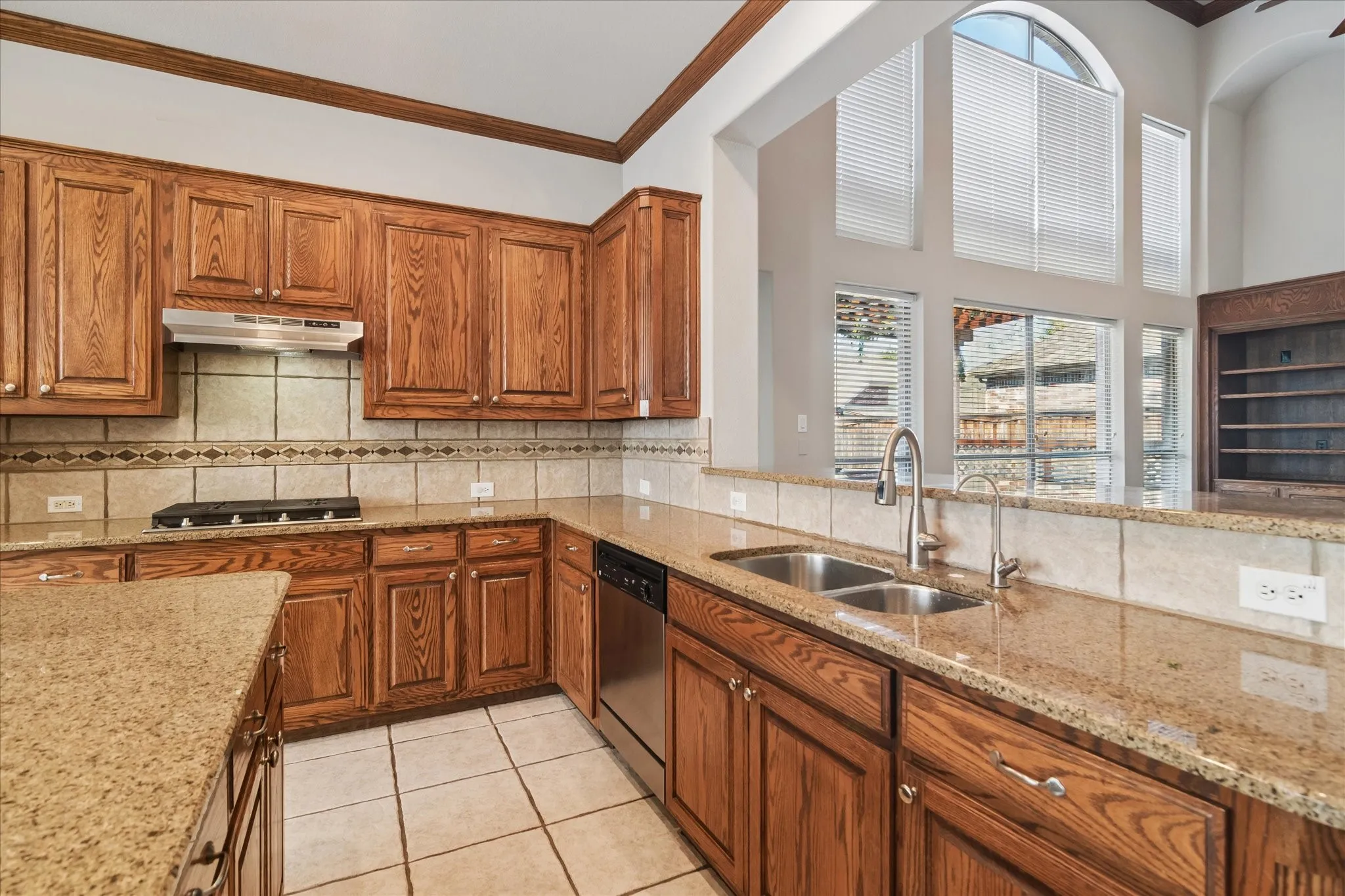 Kitchen featuring wood cabinetry, granite countertops, tile flooring, a stainless steel double basin sink, and a stainless steel dishwasher