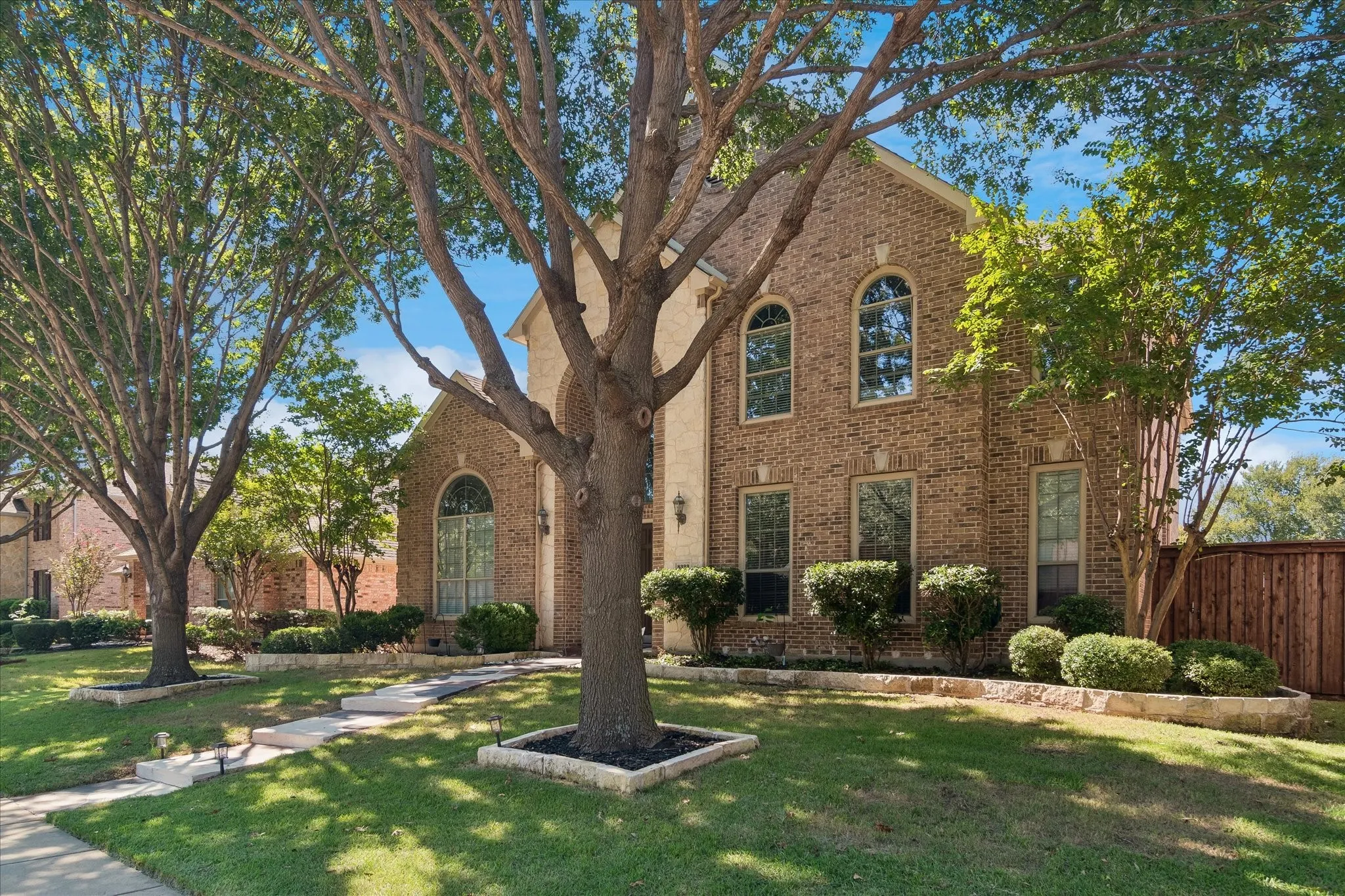 Brick facade with arched windows, mature trees, and stone-edged landscaping