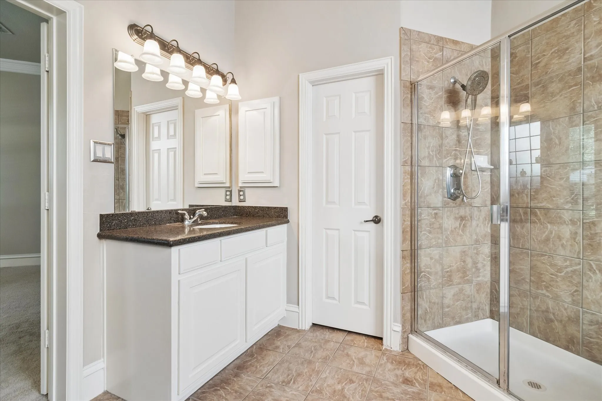 Glass-enclosed shower with tiled walls, white vanity with a dark countertop, integrated sink, and overhead lighting fixture