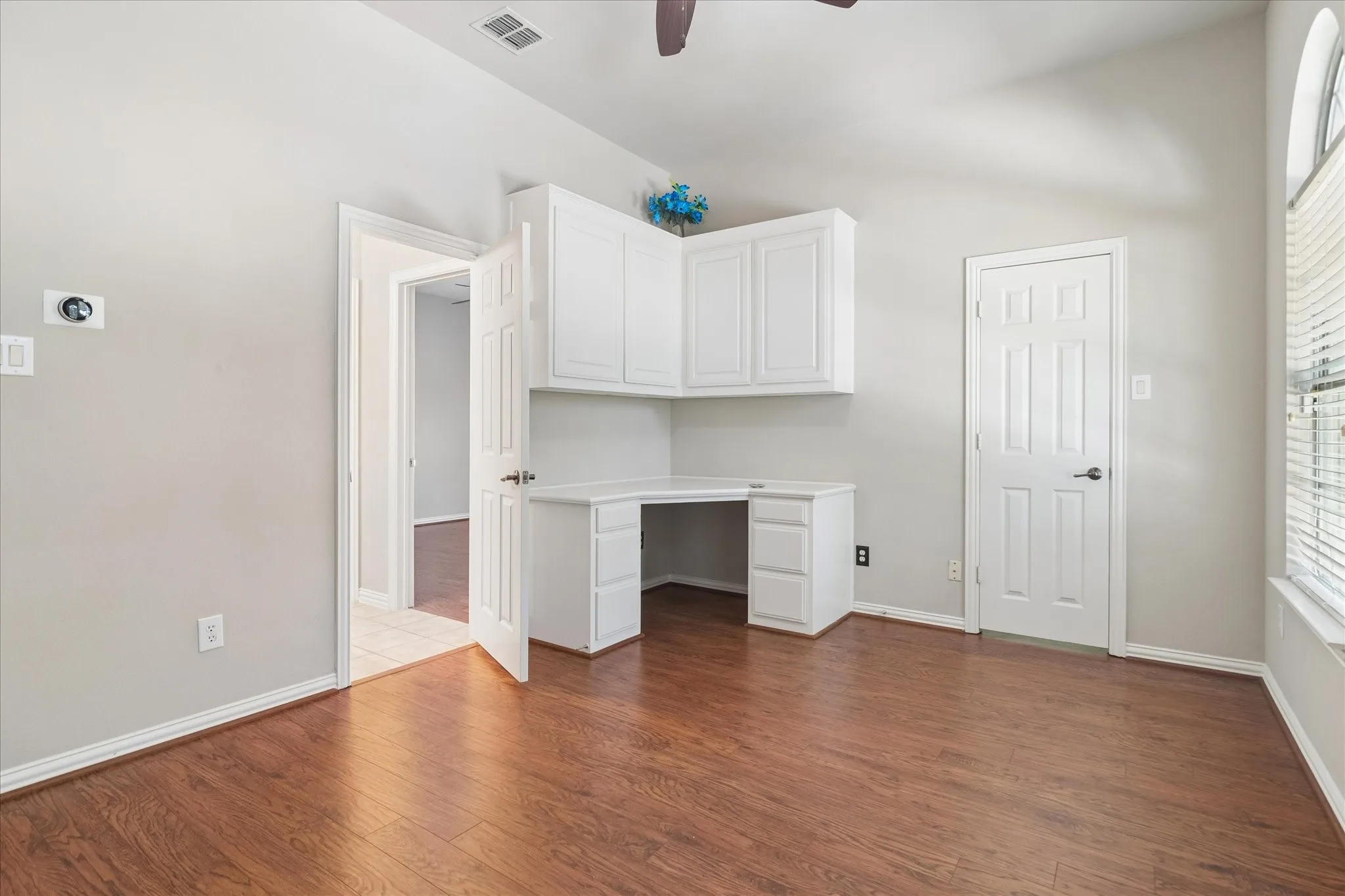 Built-in corner desk with upper and lower cabinetry, wood-finish flooring, vaulted ceiling, and an arched window