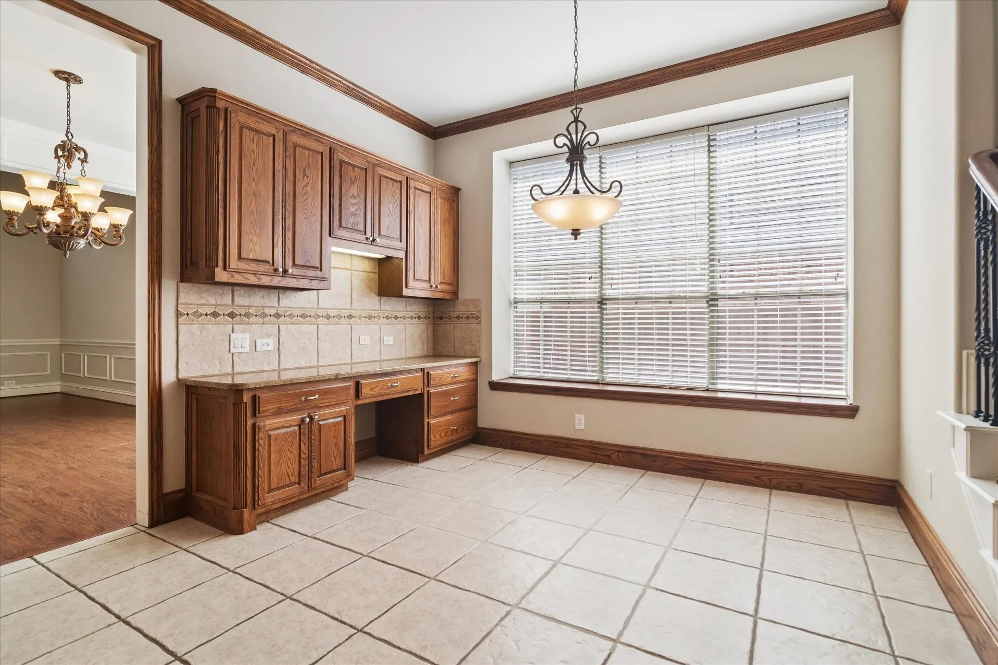Built-in wood cabinetry with integrated desk space, ceramic tile flooring, large window with blinds, and decorative light fixture