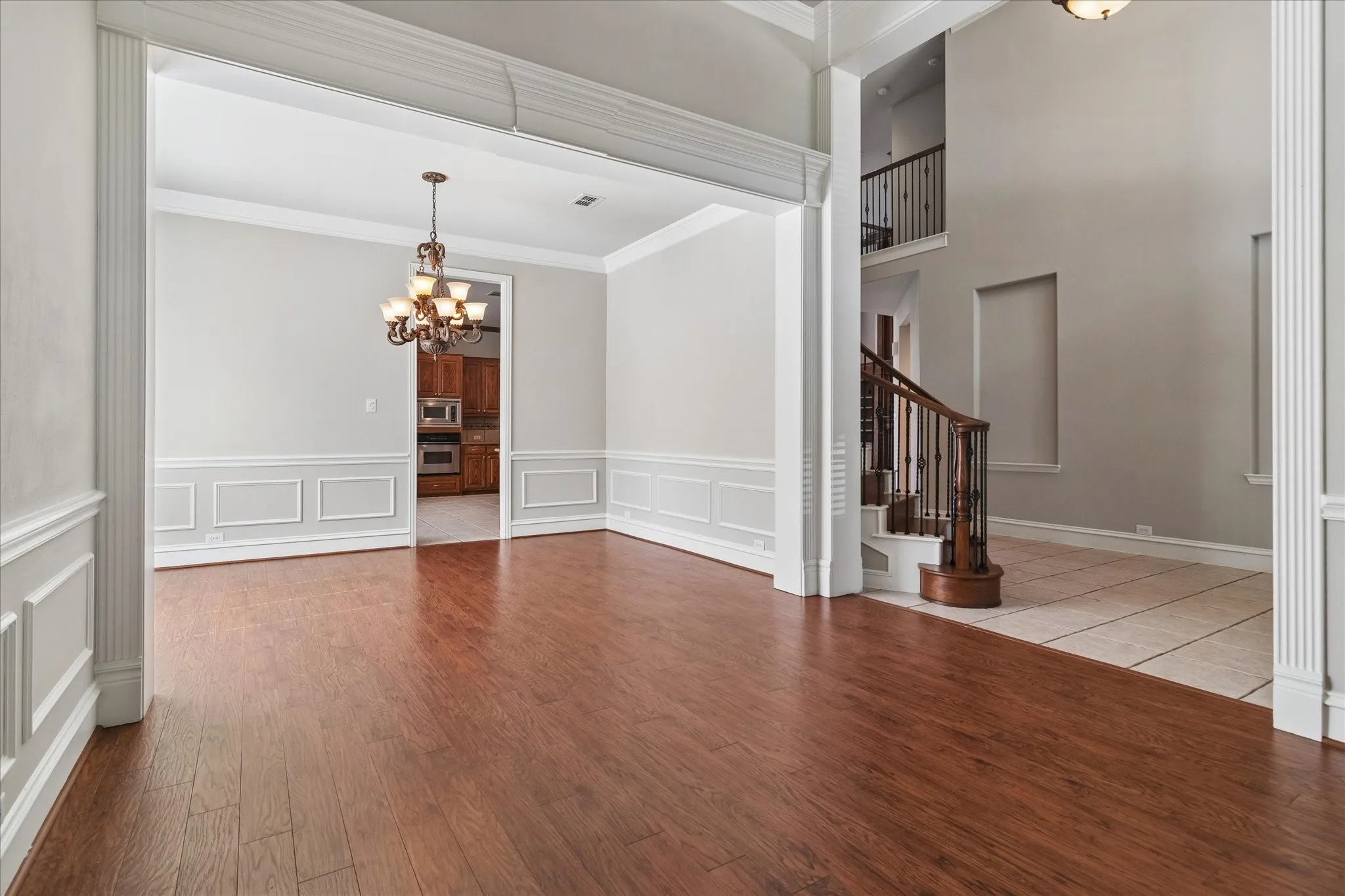 Hardwood-finish flooring, decorative wainscoting, chandelier lighting, arched entryway, and a grand staircase with dark wood railings