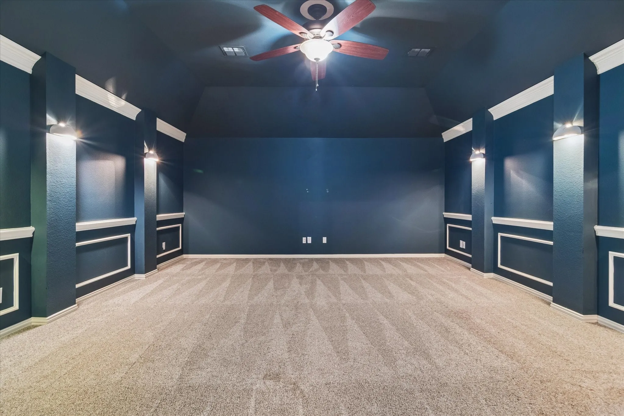 Carpeted room featuring a ceiling fan with integrated lighting, wall sconces, and decorative wall molding