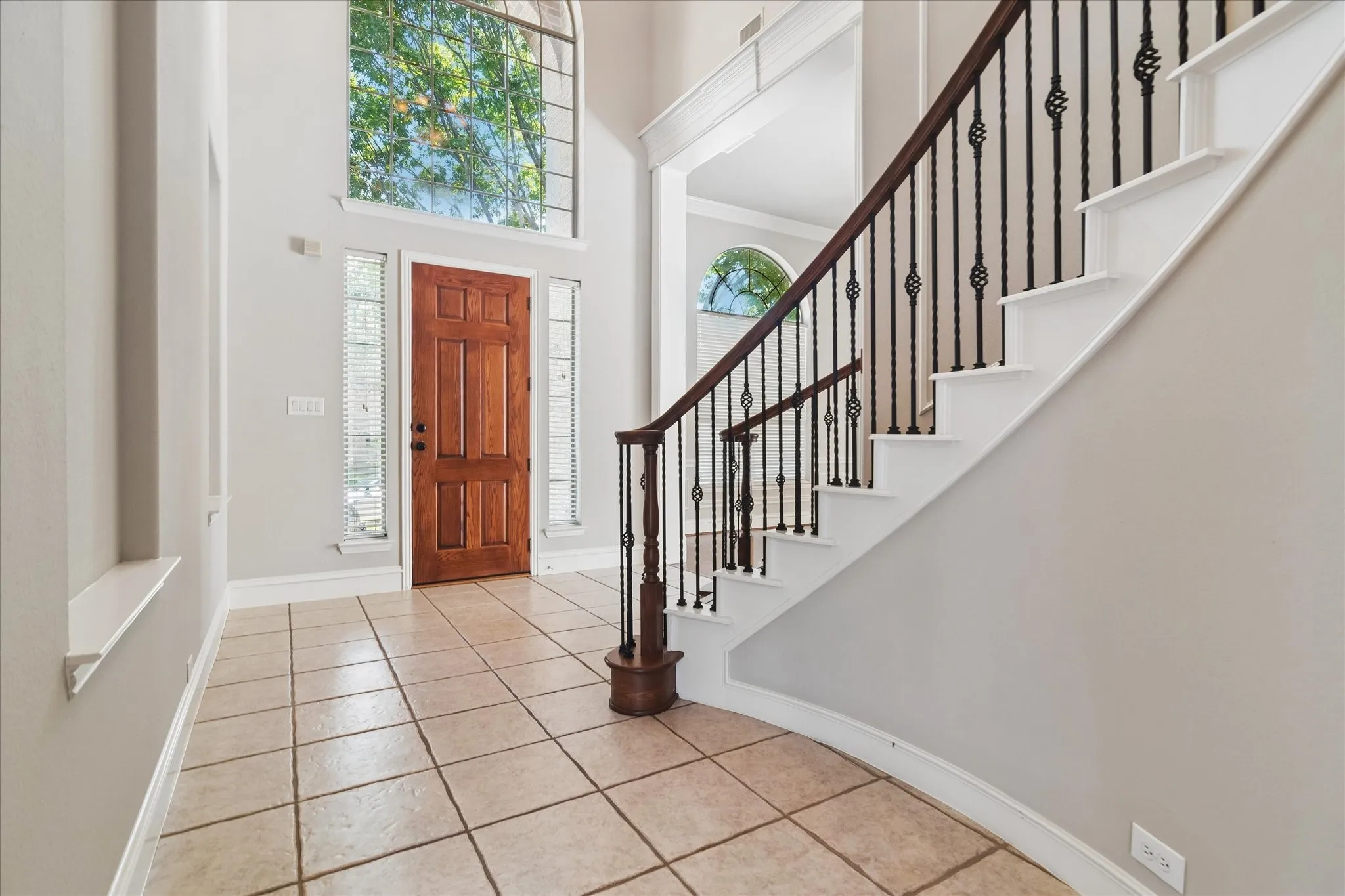 Two-story foyer with a natural wood paneled door, arched transom window, and tile flooring