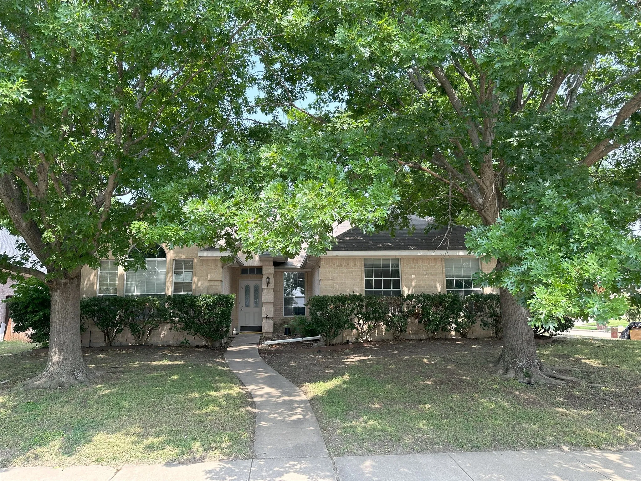 Traditional-style exterior with a covered entry, concrete pathway, established trees, and mature landscaping