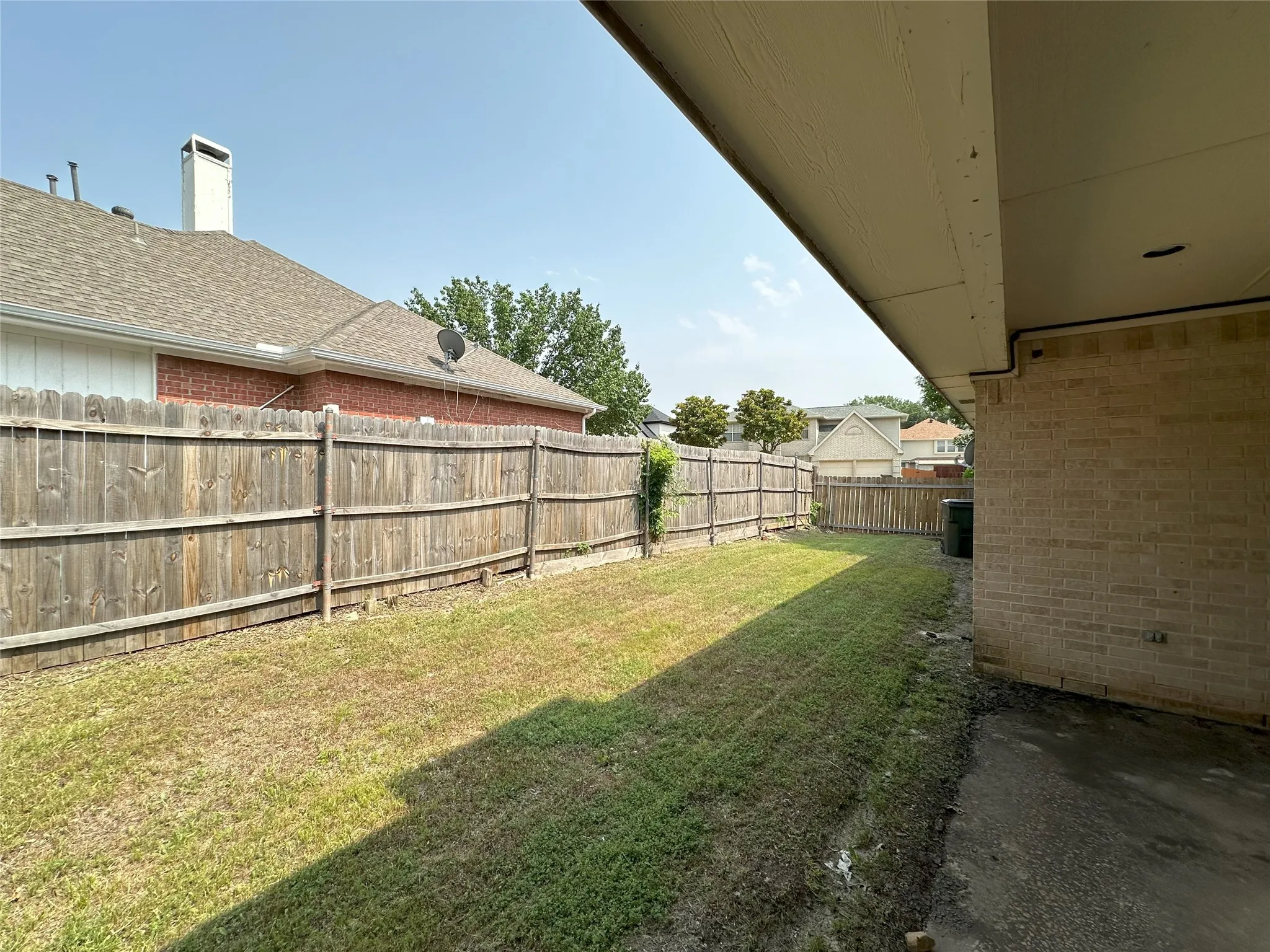Expansive backyard featuring a wood fence, a covered patio area, and a large grass lawn