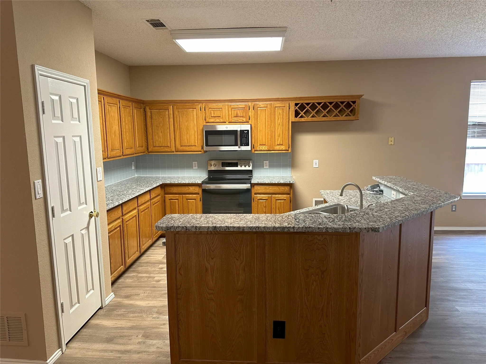 Kitchen featuring wood-finish cabinetry, granite-style countertops, stainless steel appliances, a built-in wine rack, and wood-finish flooring