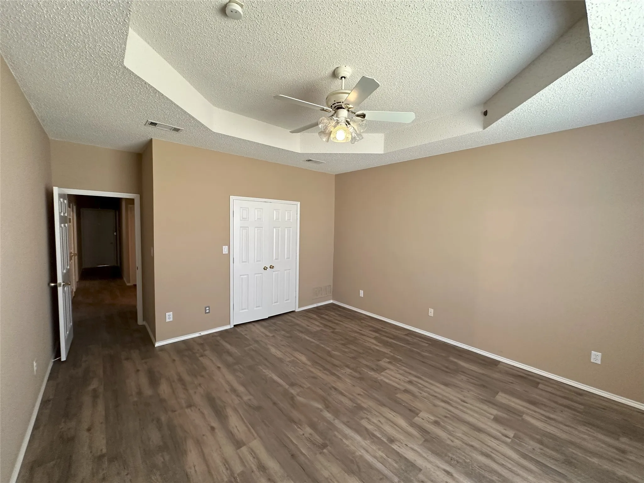 Tray ceiling featuring a built-in ceiling fan, wood-finish flooring, and a double-door closet