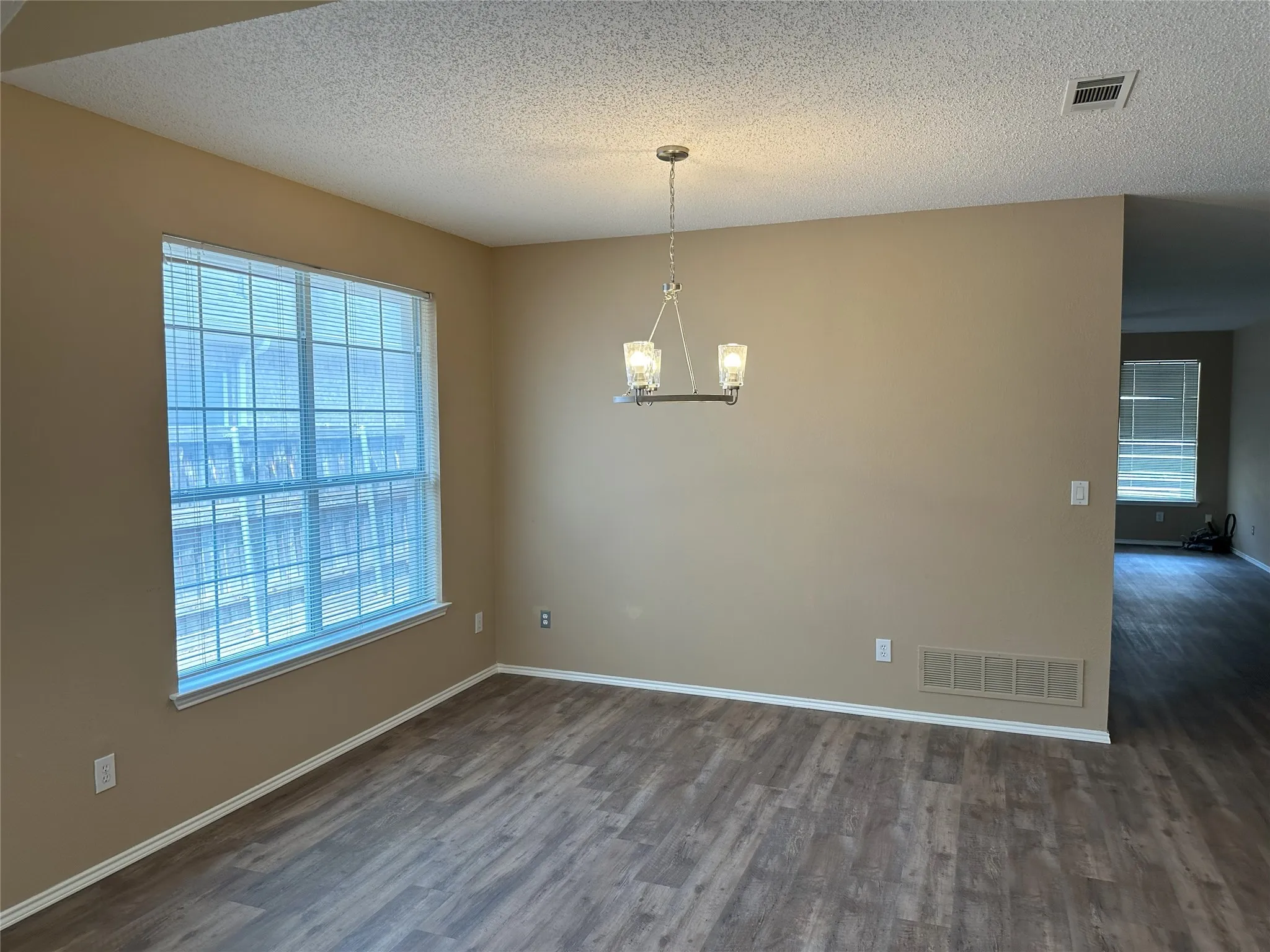 Wood-finish flooring throughout, large window with blinds, and a contemporary chandelier