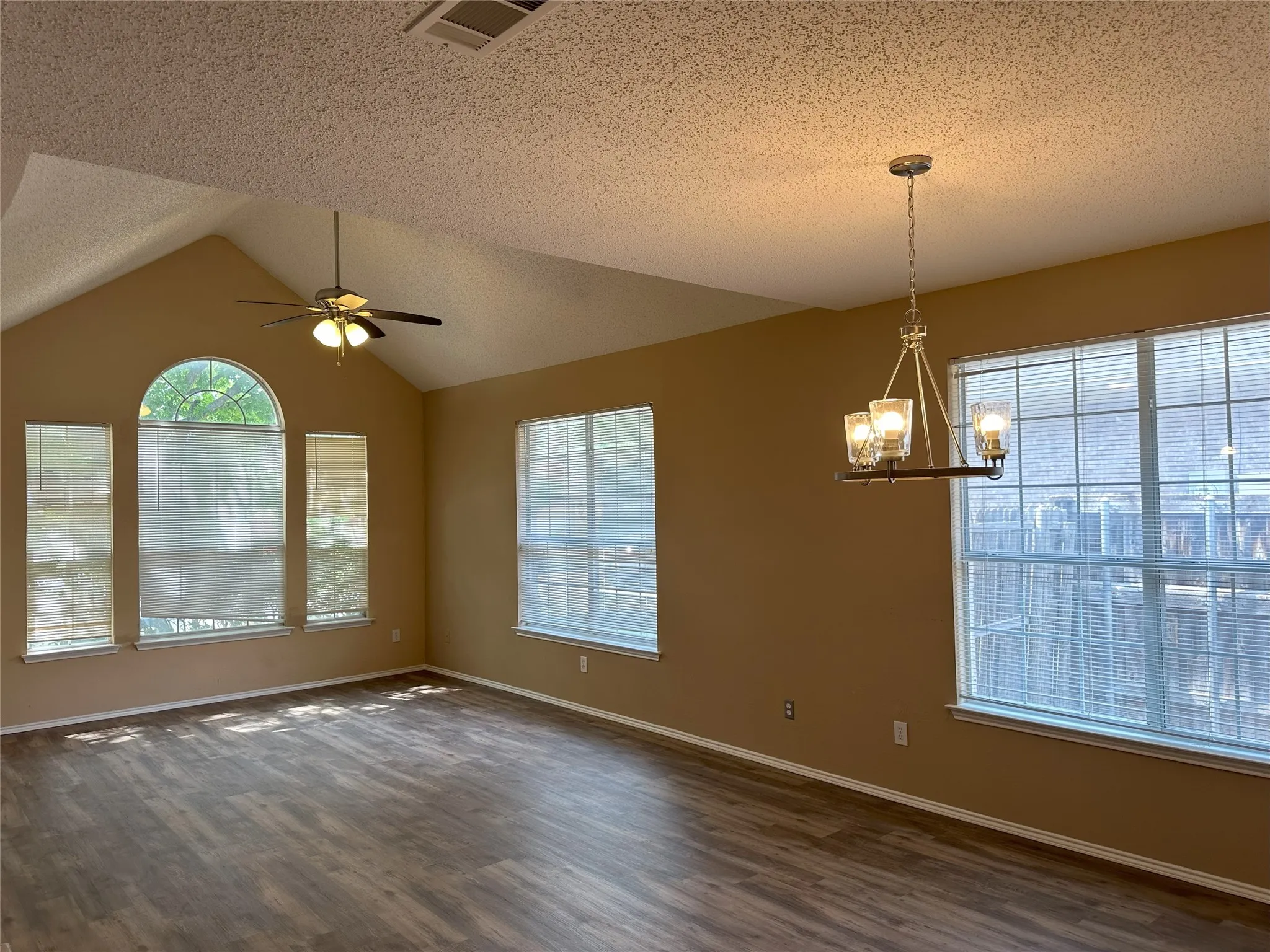 Vaulted ceiling with a ceiling fan, wood-finish flooring, and multiple windows including an arched window