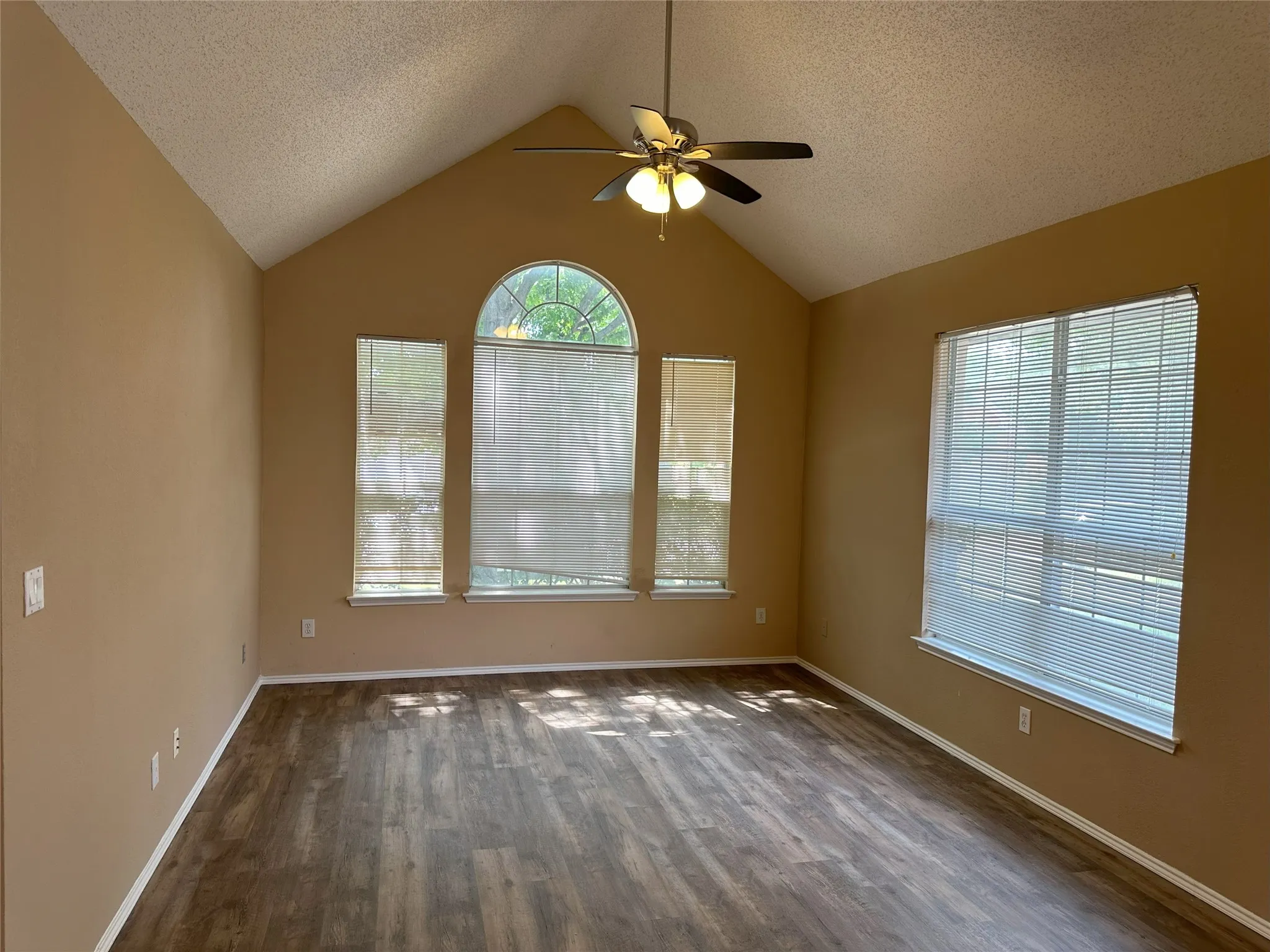 Vaulted ceiling with a ceiling fan, wood-finish flooring, and multiple windows