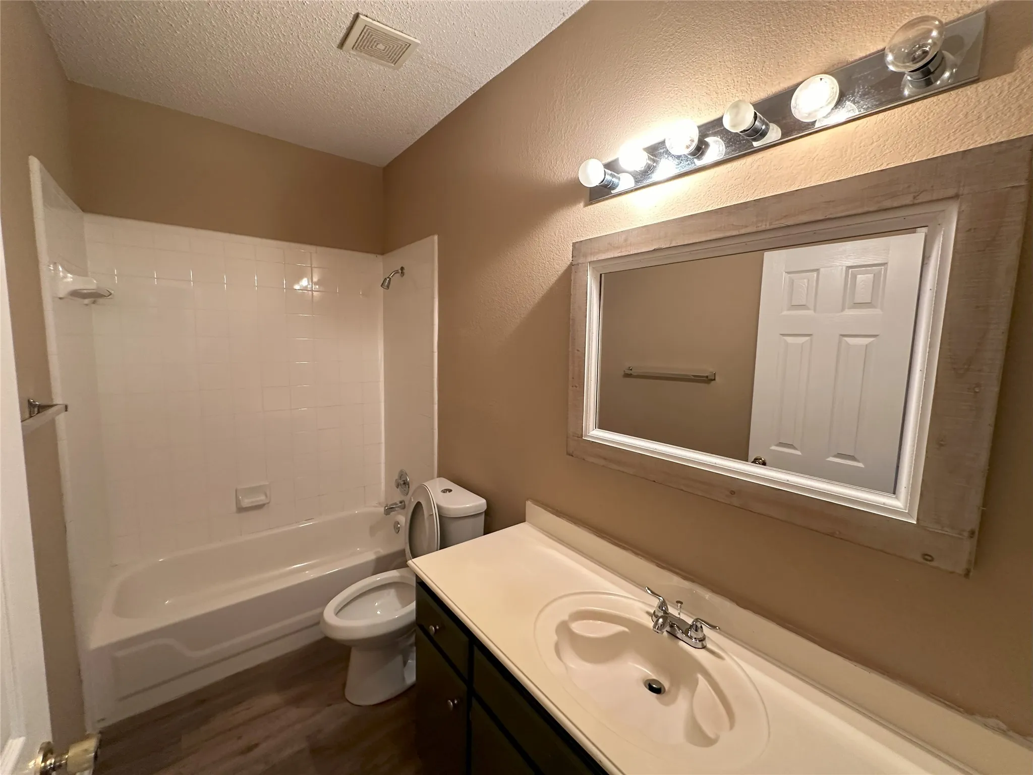 Bathroom with an integrated sink vanity, wood-finish flooring, full bathtub with shower, and a framed wall mirror