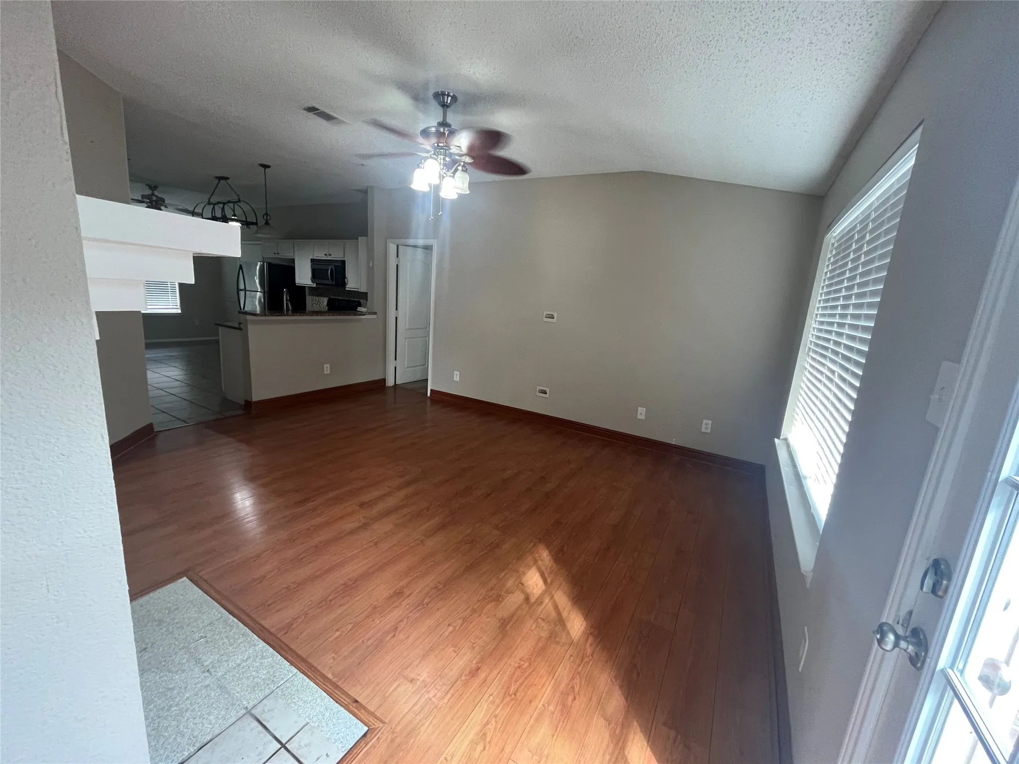 Vaulted ceiling, wood-finish flooring, ceiling fan with integrated lighting, window with blinds, and white interior door