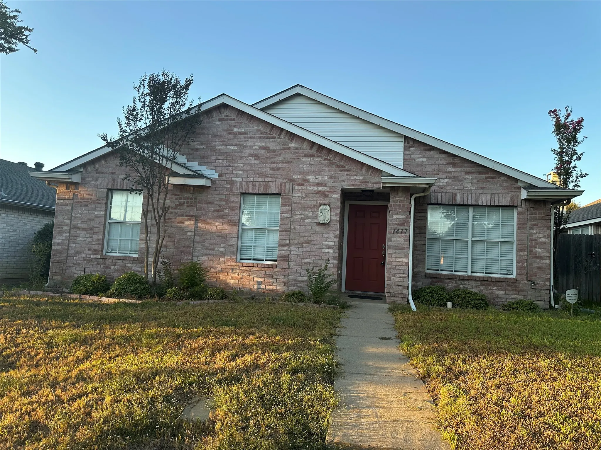Brick exterior with white window frames, a red entry door, white gutters, and a concrete walkway