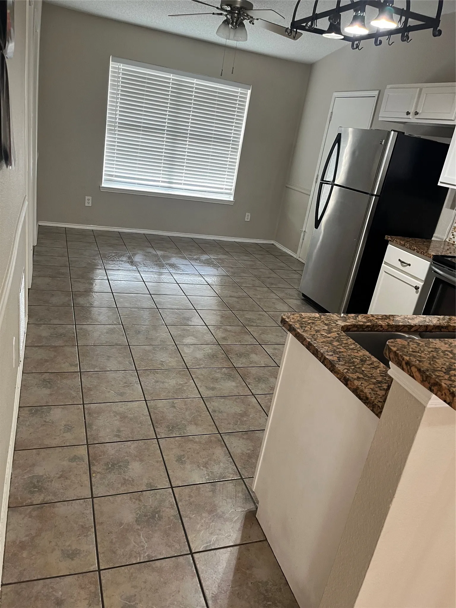 Tiled flooring throughout, ceiling fan with integrated lighting, window with blinds, white cabinetry, and stainless steel refrigerator