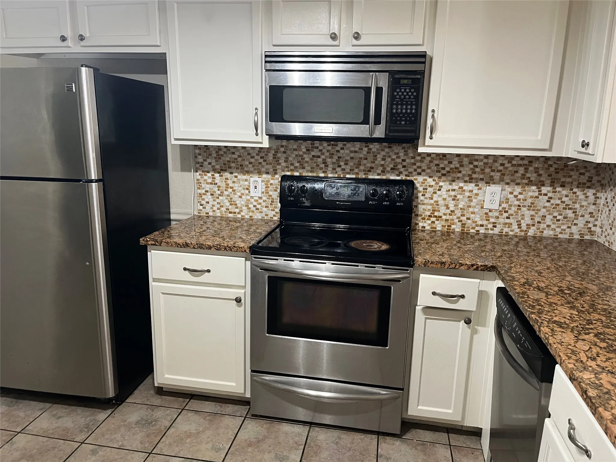 White cabinetry with brushed nickel hardware, speckled granite countertops, mosaic tile backsplash, and stainless steel appliances