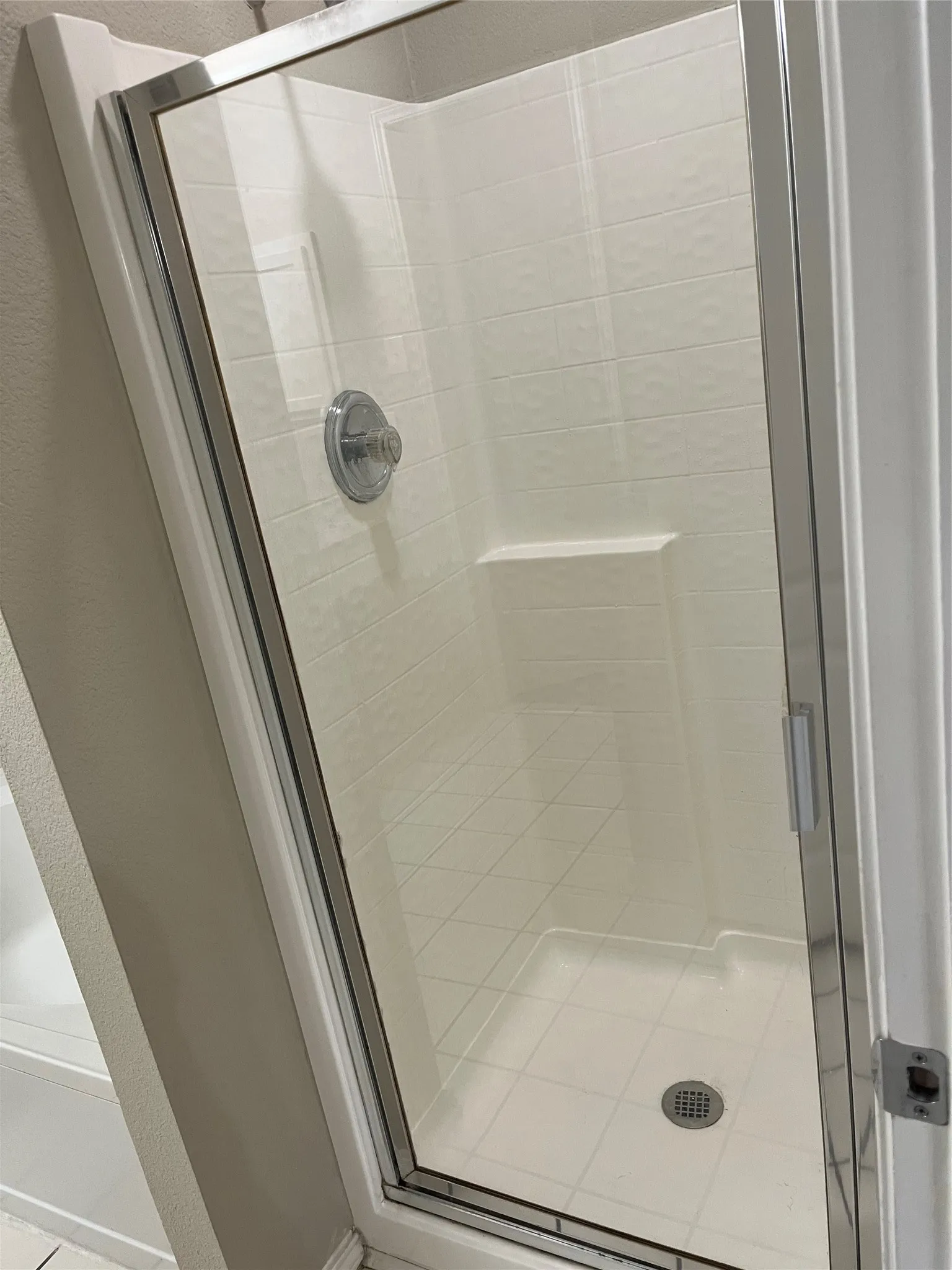 Enclosed shower featuring a clear glass door, chrome shower fixture, built-in recessed shelf, and tiled walls and floor