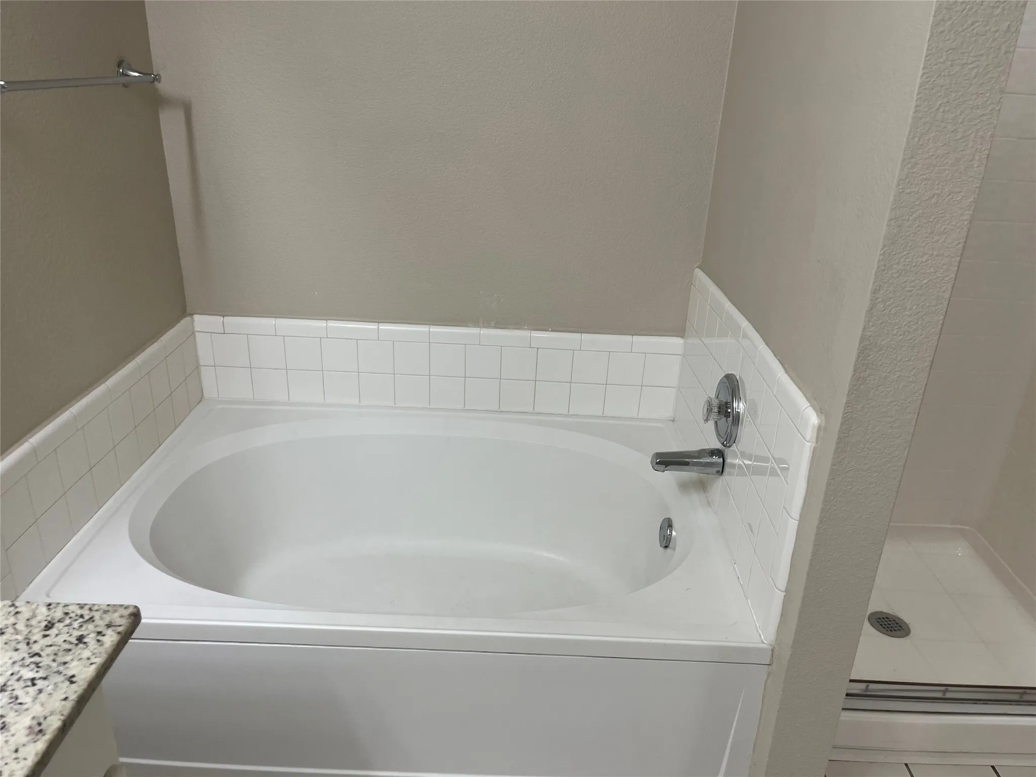 Built-in soaking tub with chrome fixtures, white subway tile surround, and an adjacent shower enclosure with tile flooring
