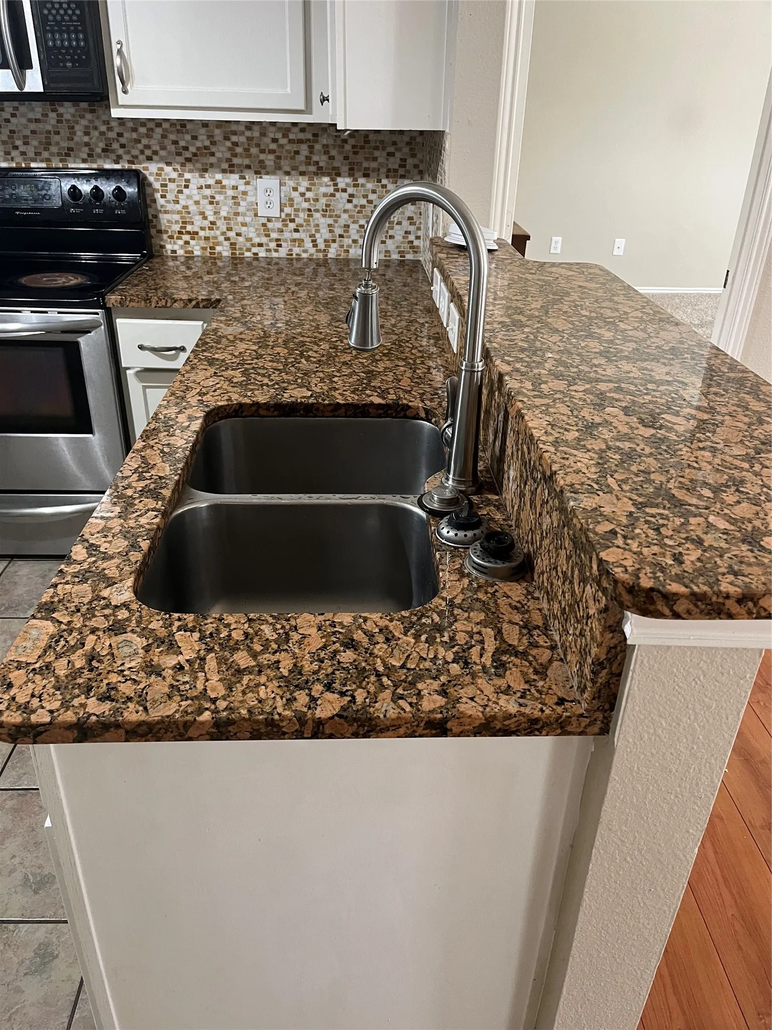 Granite-style countertops, mosaic tile backsplash, stainless steel double basin sink, and a chrome gooseneck faucet