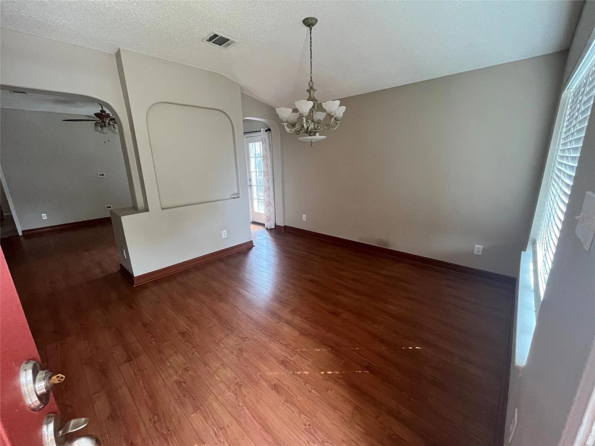 Wood-finish flooring throughout, arched wall cutout, and a single-light chandelier