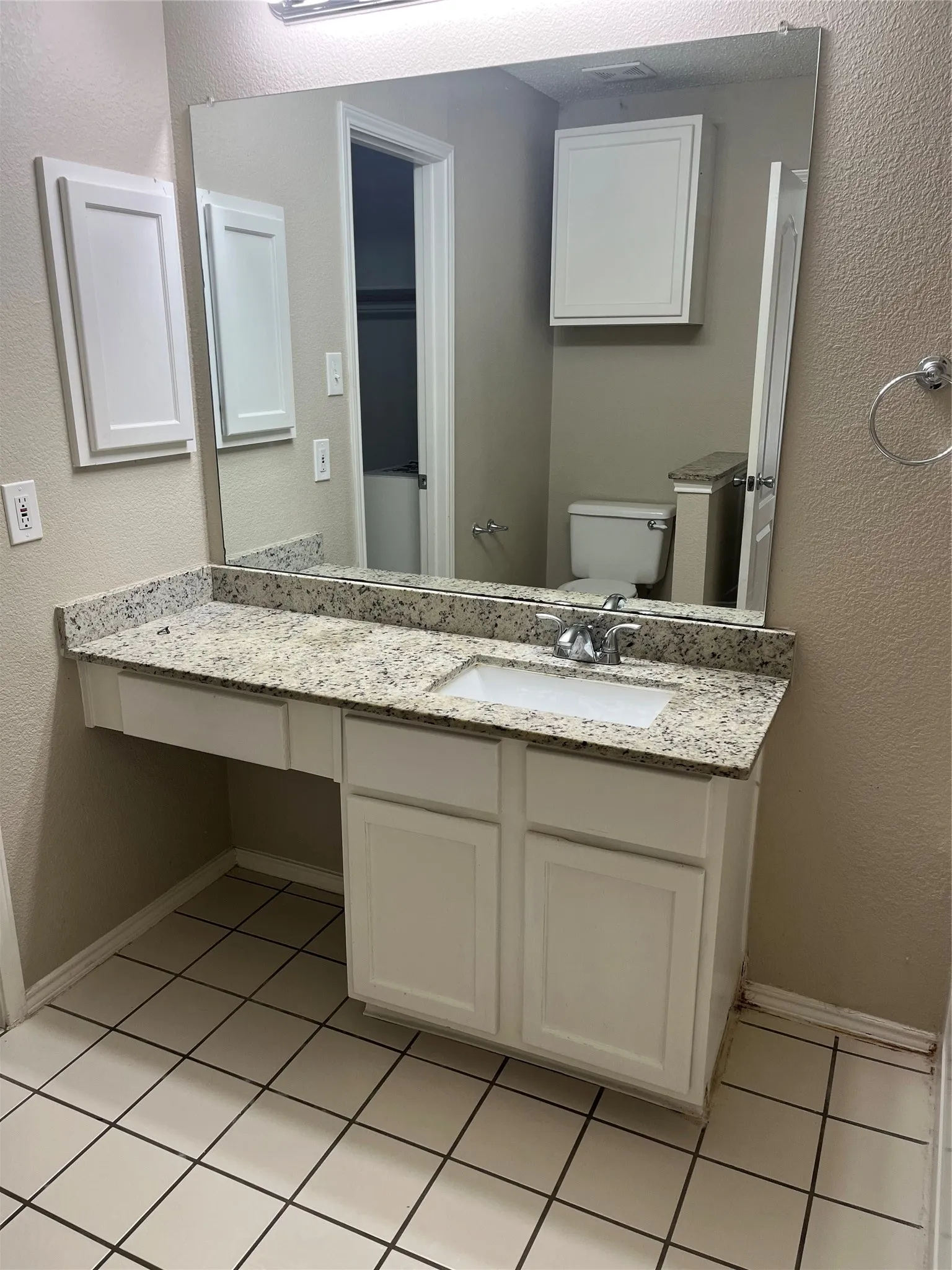 Bathroom vanity with a granite-finish countertop, under-mount sink, chrome faucet, and white cabinetry