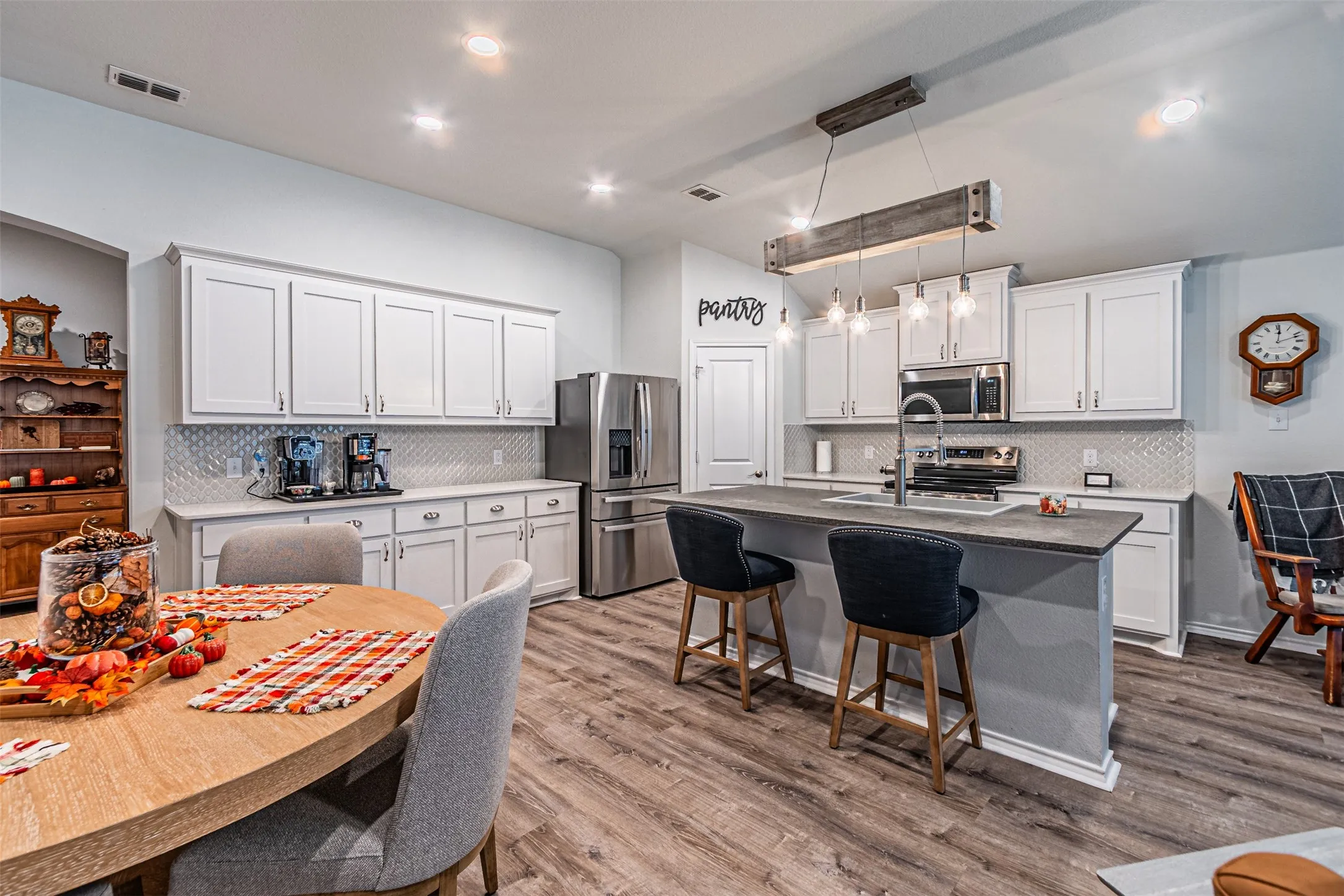 Kitchen featuring white cabinetry, stainless steel appliances, a center island with seating, wood-finish flooring, and a decorative pendant light fixture