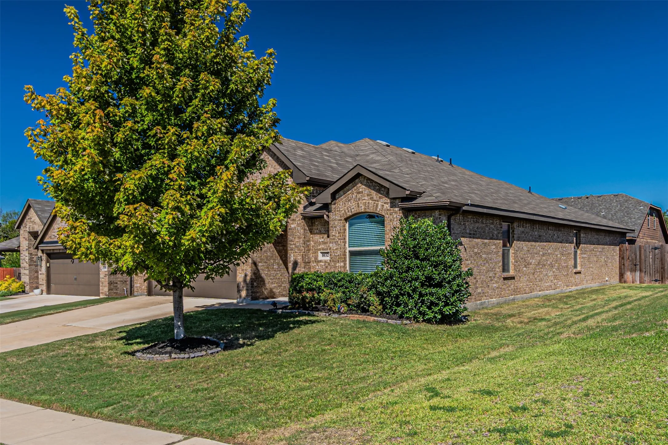 Brick exterior with dark shingle roofing, arched window, and mature landscaping