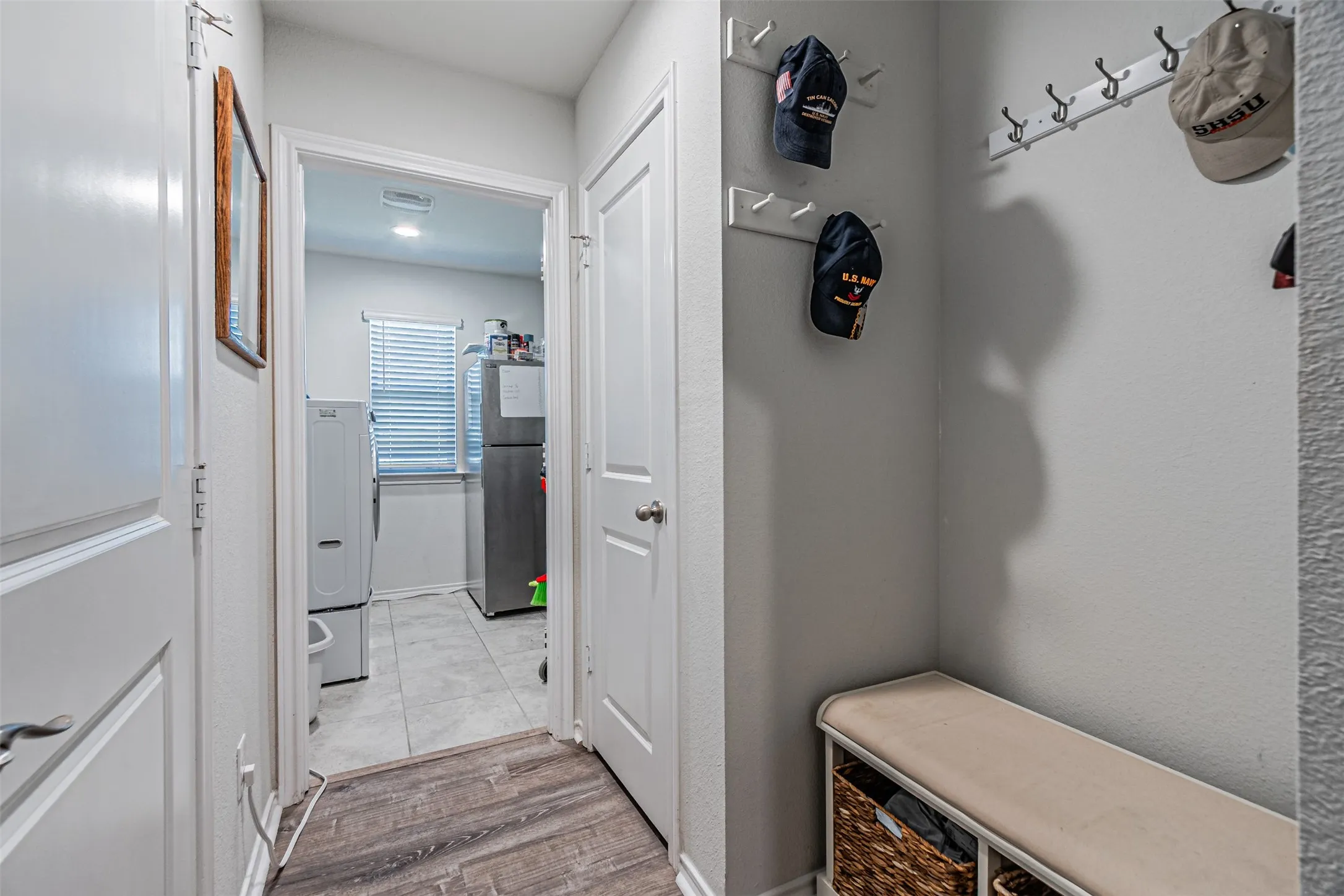 Wood-finish flooring leading to a tiled room, featuring an interior window with blinds