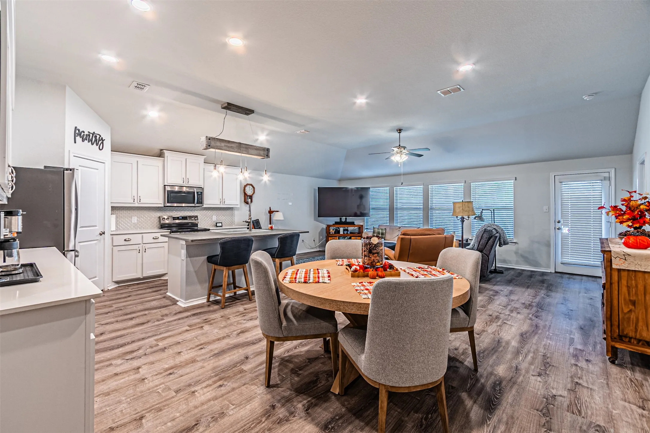 Open-concept living space with wood-finish flooring, white cabinetry, a kitchen island, stainless steel appliances, and a vaulted ceiling