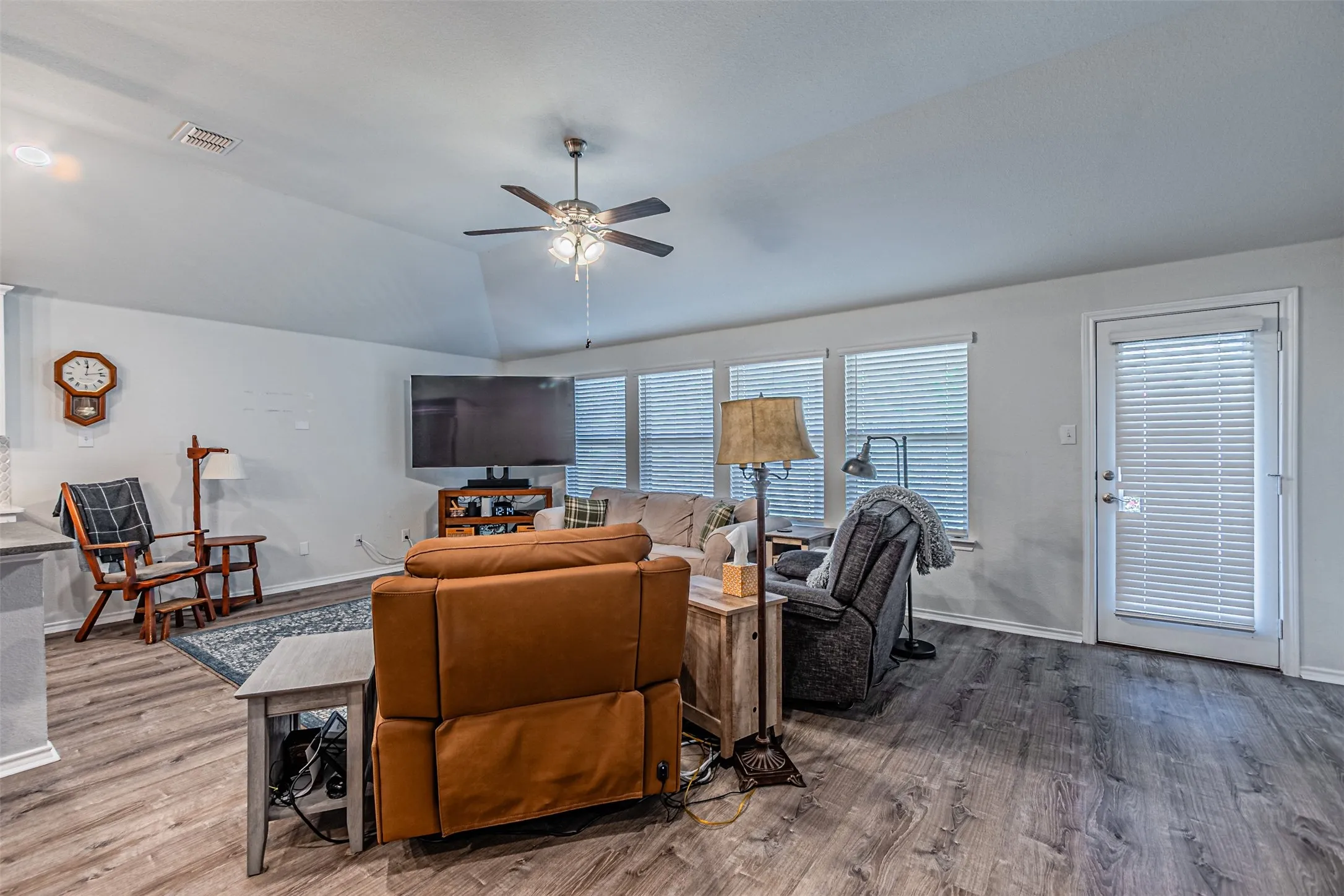Vaulted ceiling with a ceiling fan, wood-finish flooring, multiple windows with blinds, and a glass-paneled door