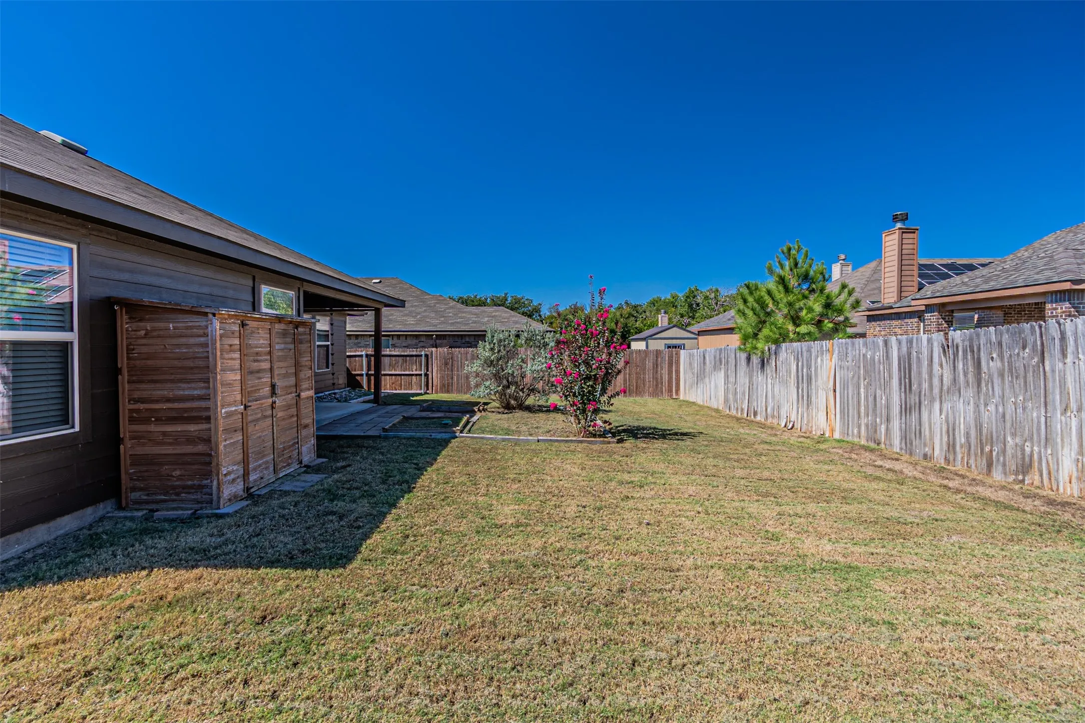 Expansive backyard featuring a covered patio, wood fencing, and a mature flowering shrub