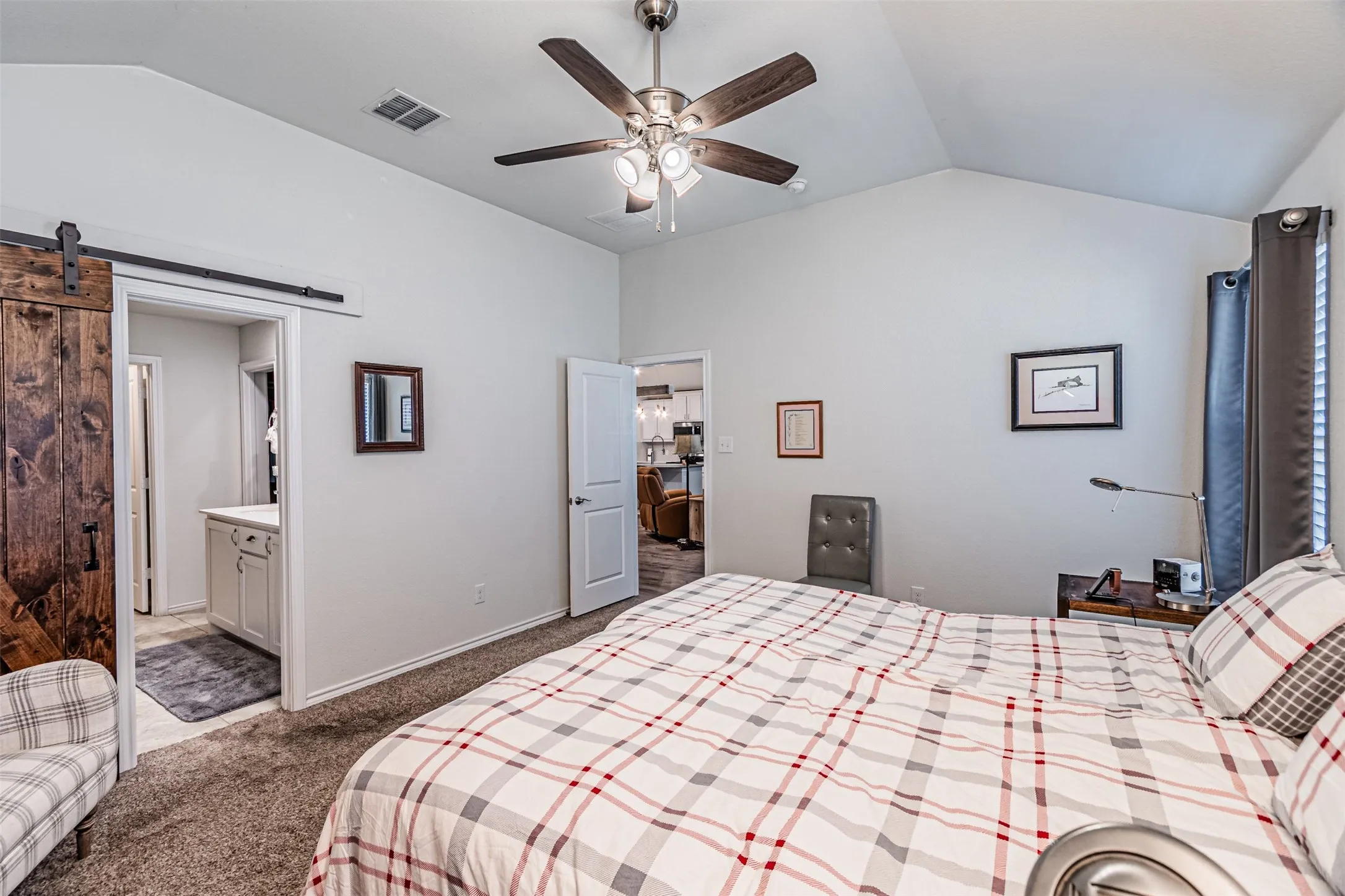 Vaulted ceiling, ceiling fan, carpet flooring, and a wood-finish barn door