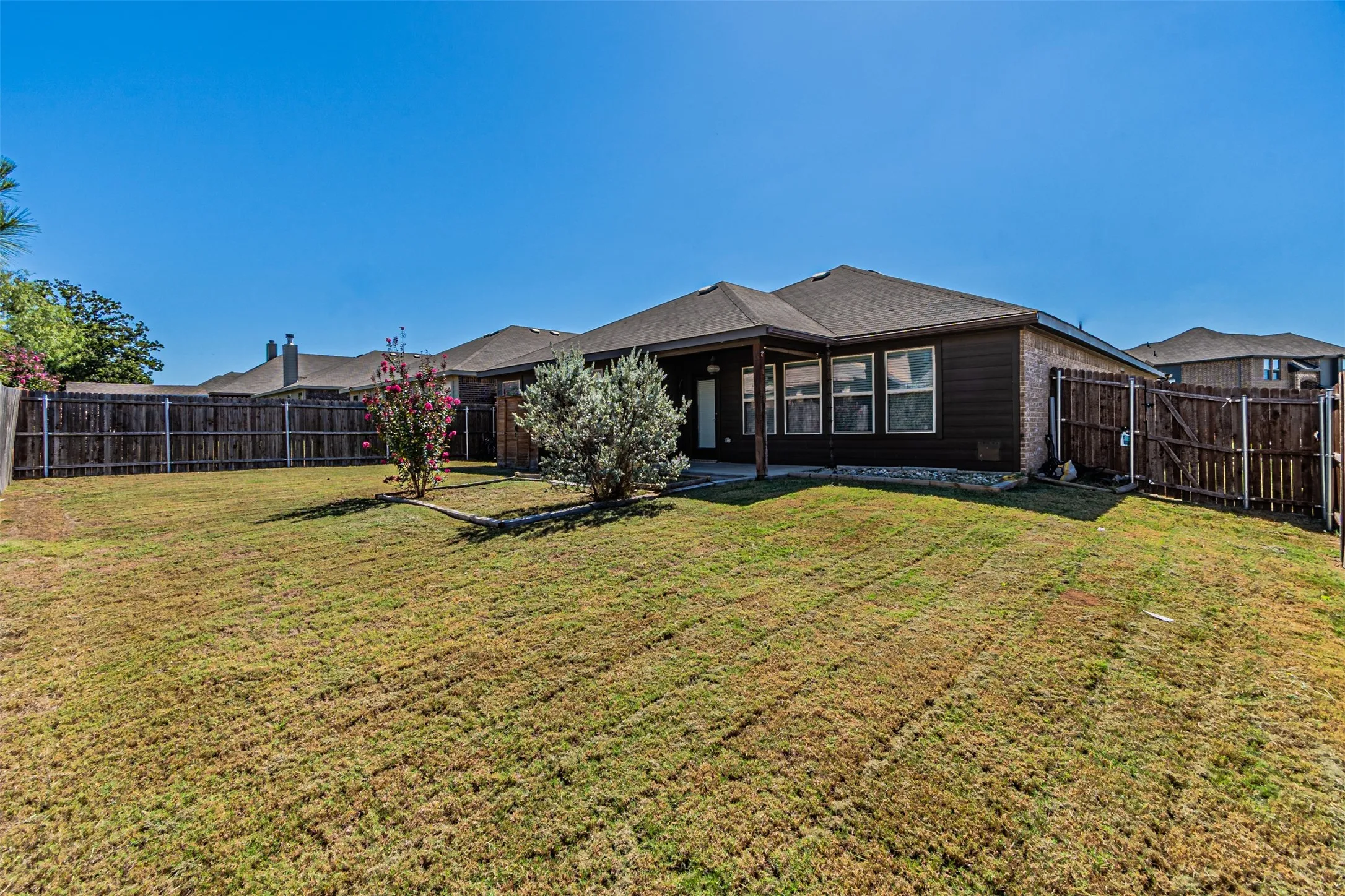 Expansive backyard featuring a manicured lawn, full privacy fencing, and a covered patio area
