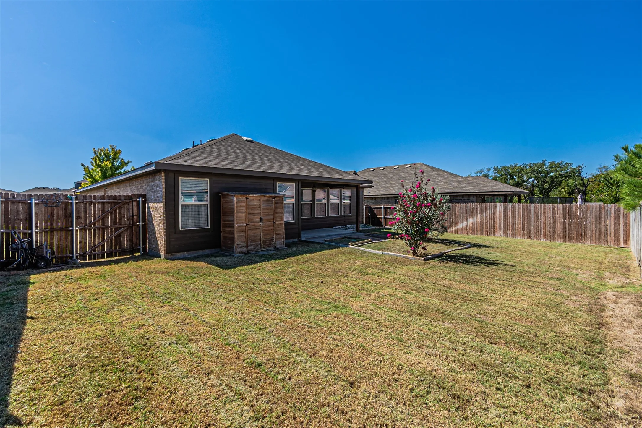 Expansive backyard with a manicured lawn, full privacy fencing, brick exterior, and a mature flowering tree
