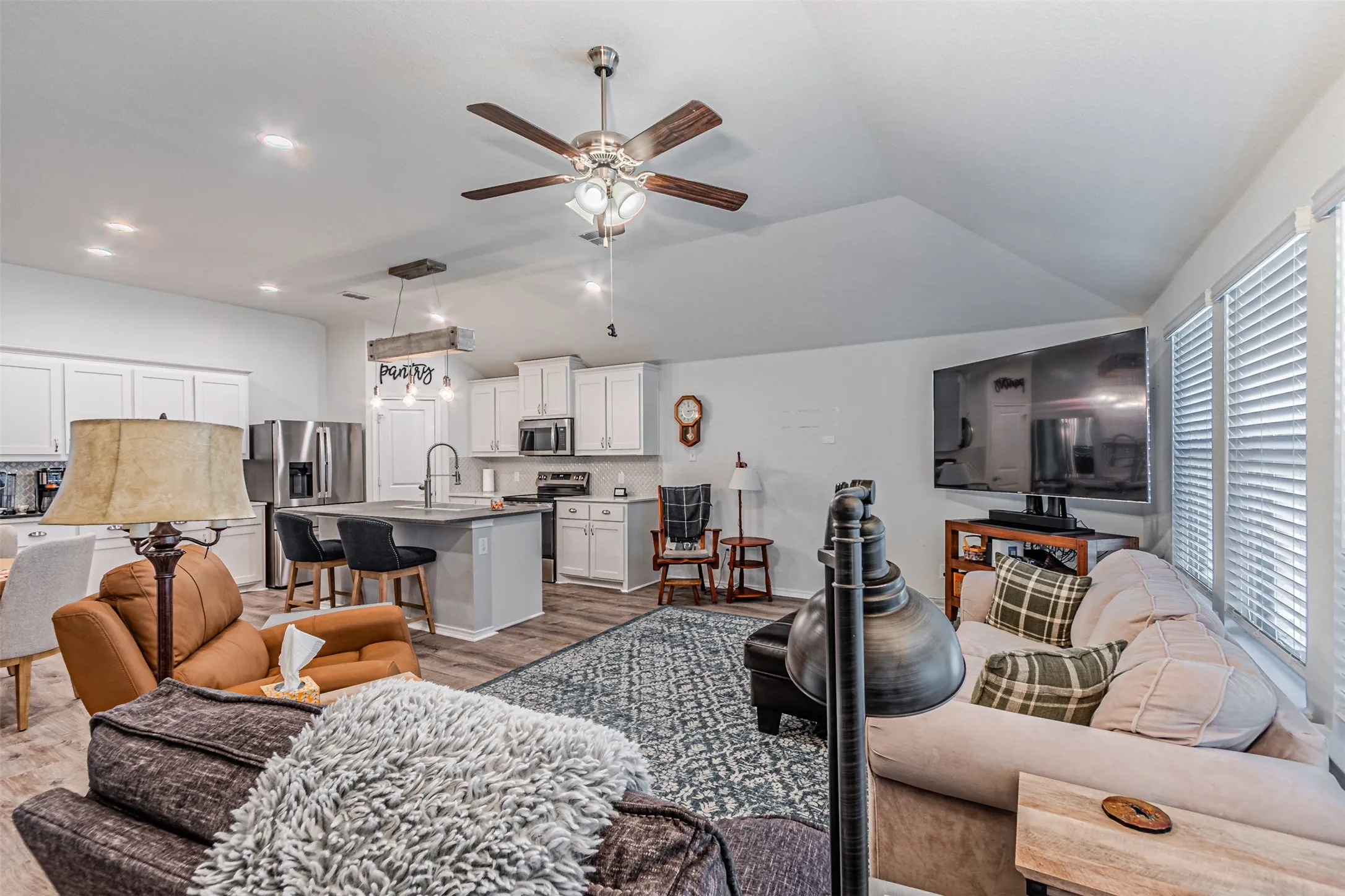 Open-concept living area featuring a vaulted ceiling with a ceiling fan, wood-finish flooring, and white window blinds