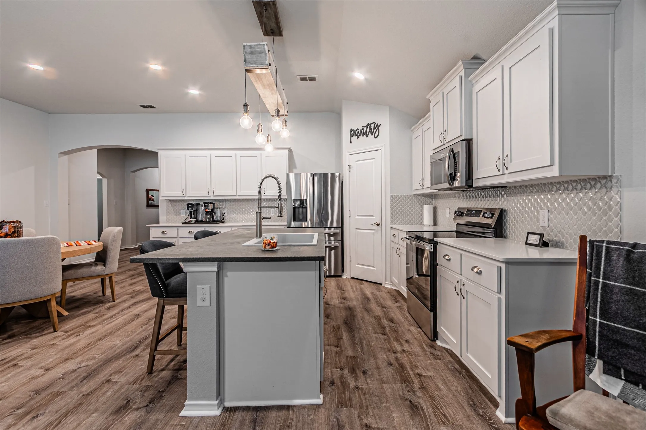 Kitchen featuring white cabinetry, wood-finish flooring, a central island with an undermount sink, stainless steel appliances, and an arched doorway