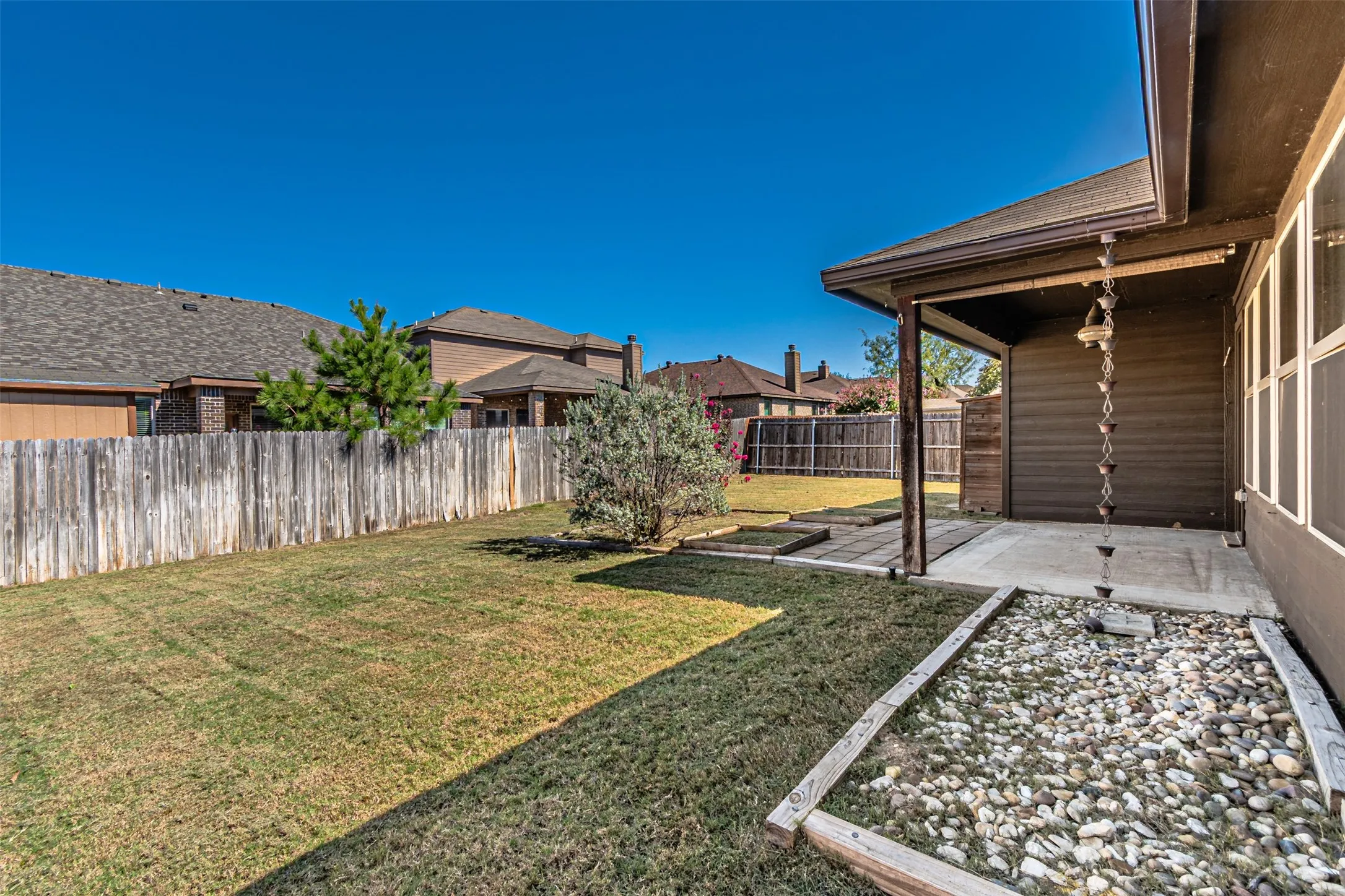Covered patio with concrete flooring, framed by a wooden privacy fence and a rock garden