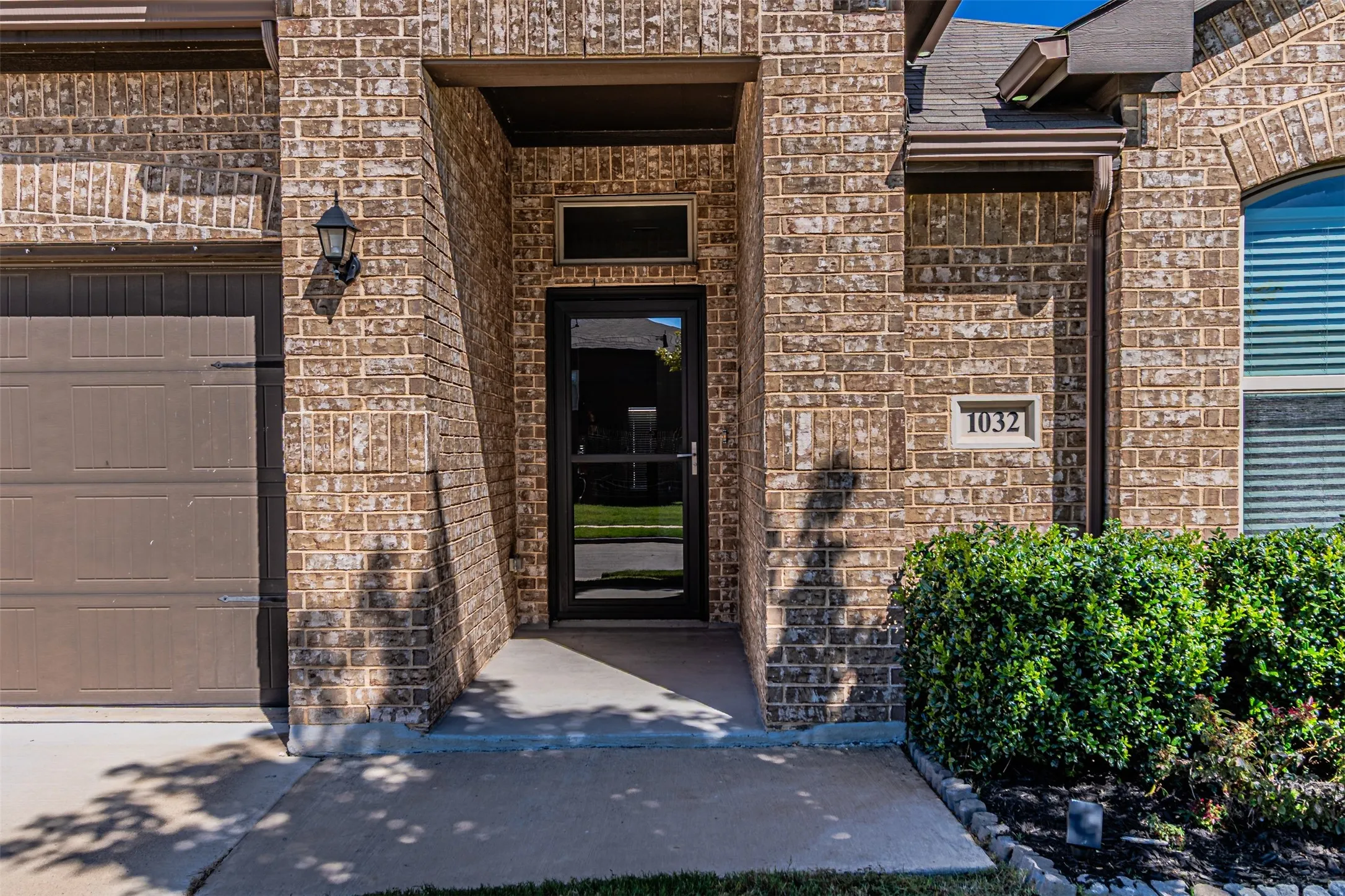 Brick exterior with a dark-framed entry door, front porch lighting, and a paved walkway
