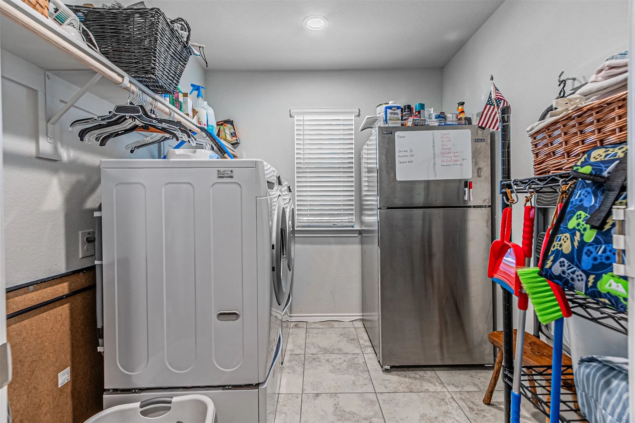 Laundry area featuring a window with blinds, tile flooring, and overhead shelving