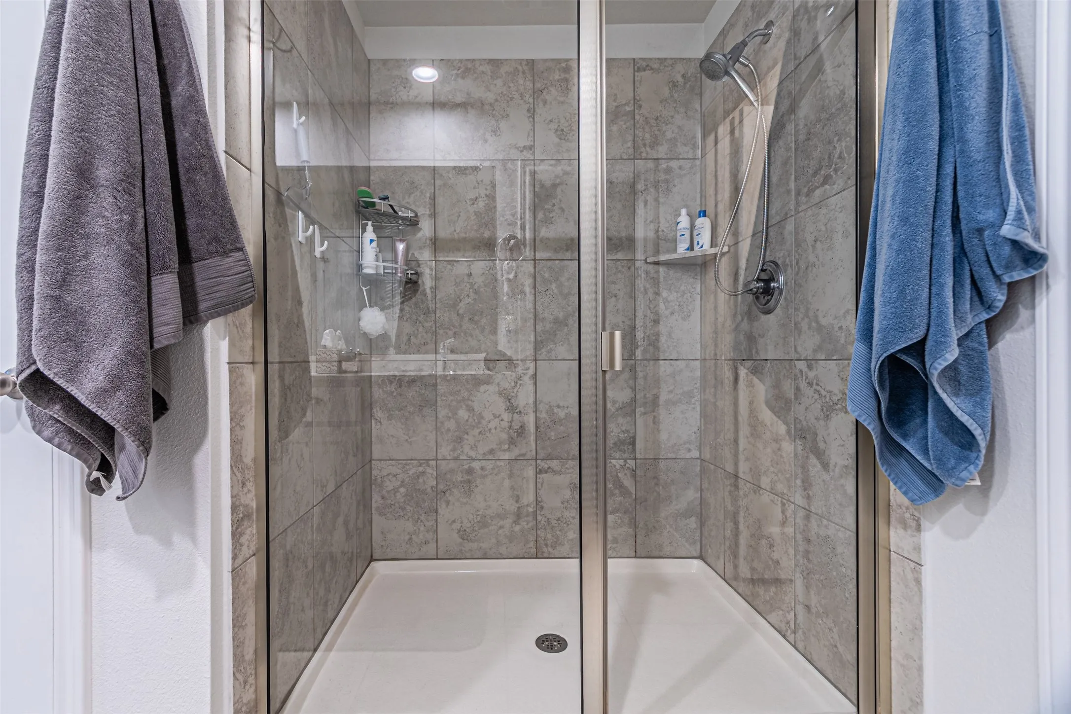 Enclosed shower featuring glass doors, a fixed shower head, tiled walls, and a recessed ceiling light