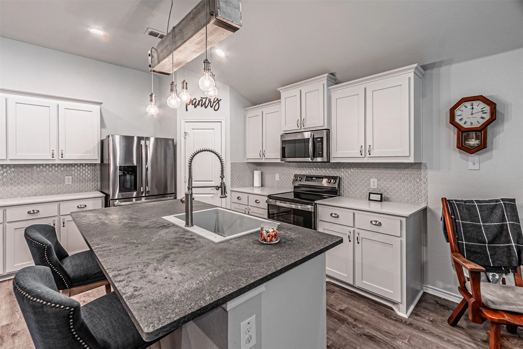 Kitchen featuring a spacious island with an integrated sink, stainless steel appliances, white cabinetry, and a patterned backsplash