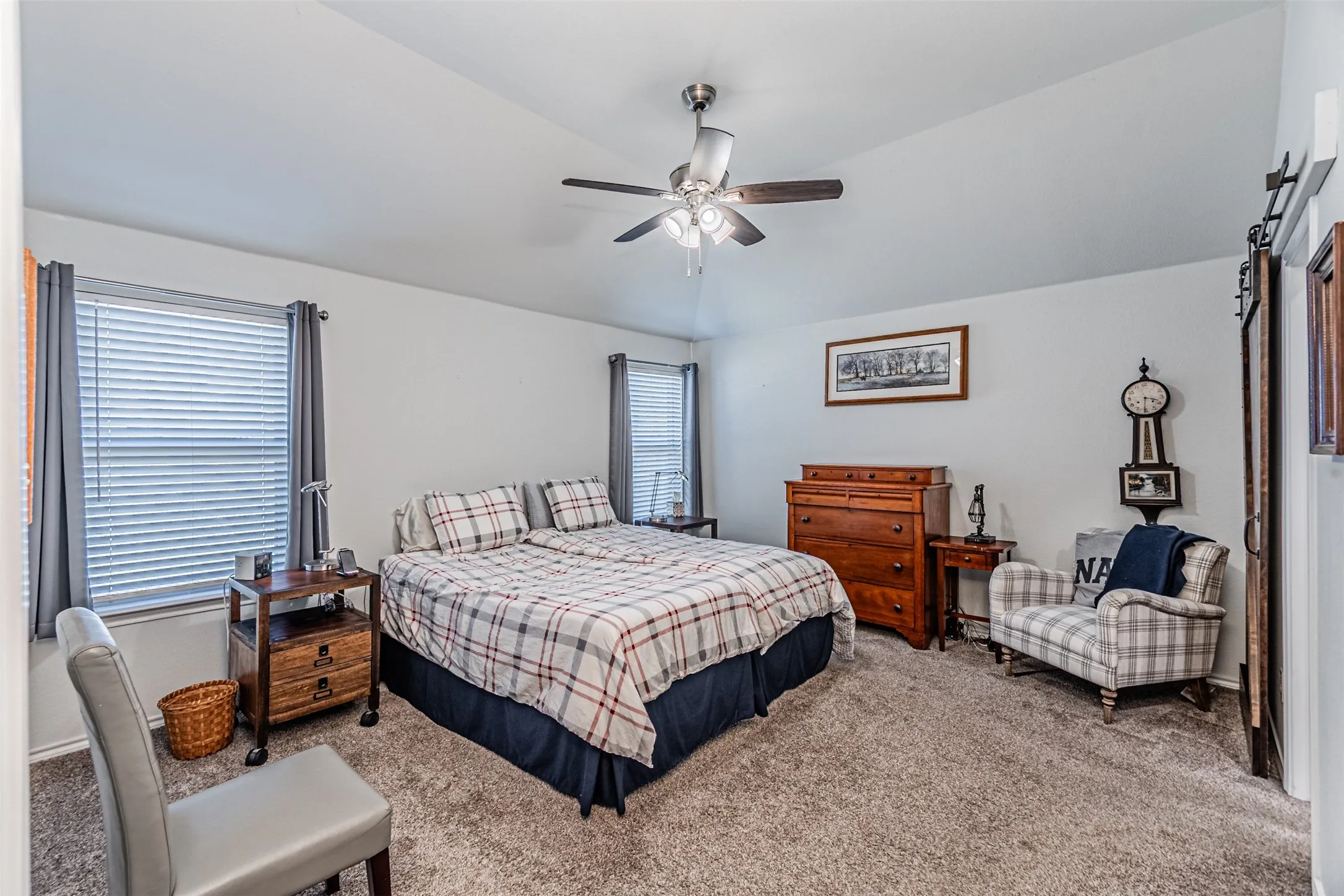 Vaulted ceiling with a ceiling fan, two windows, and carpet flooring