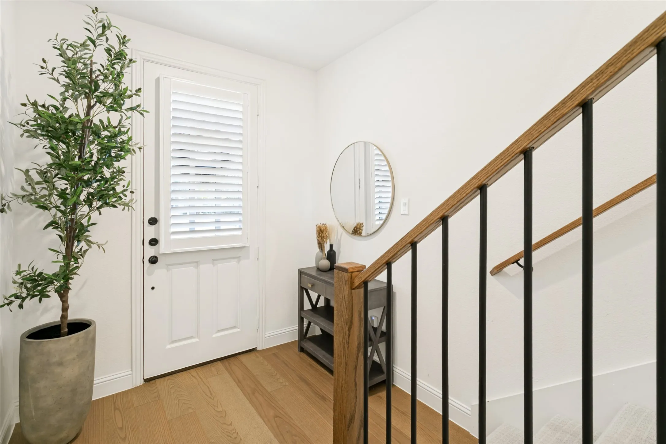 Entryway featuring a white paneled door with louvered window, matte black hardware, wood-finish flooring, and a staircase with wood handrails and black balusters