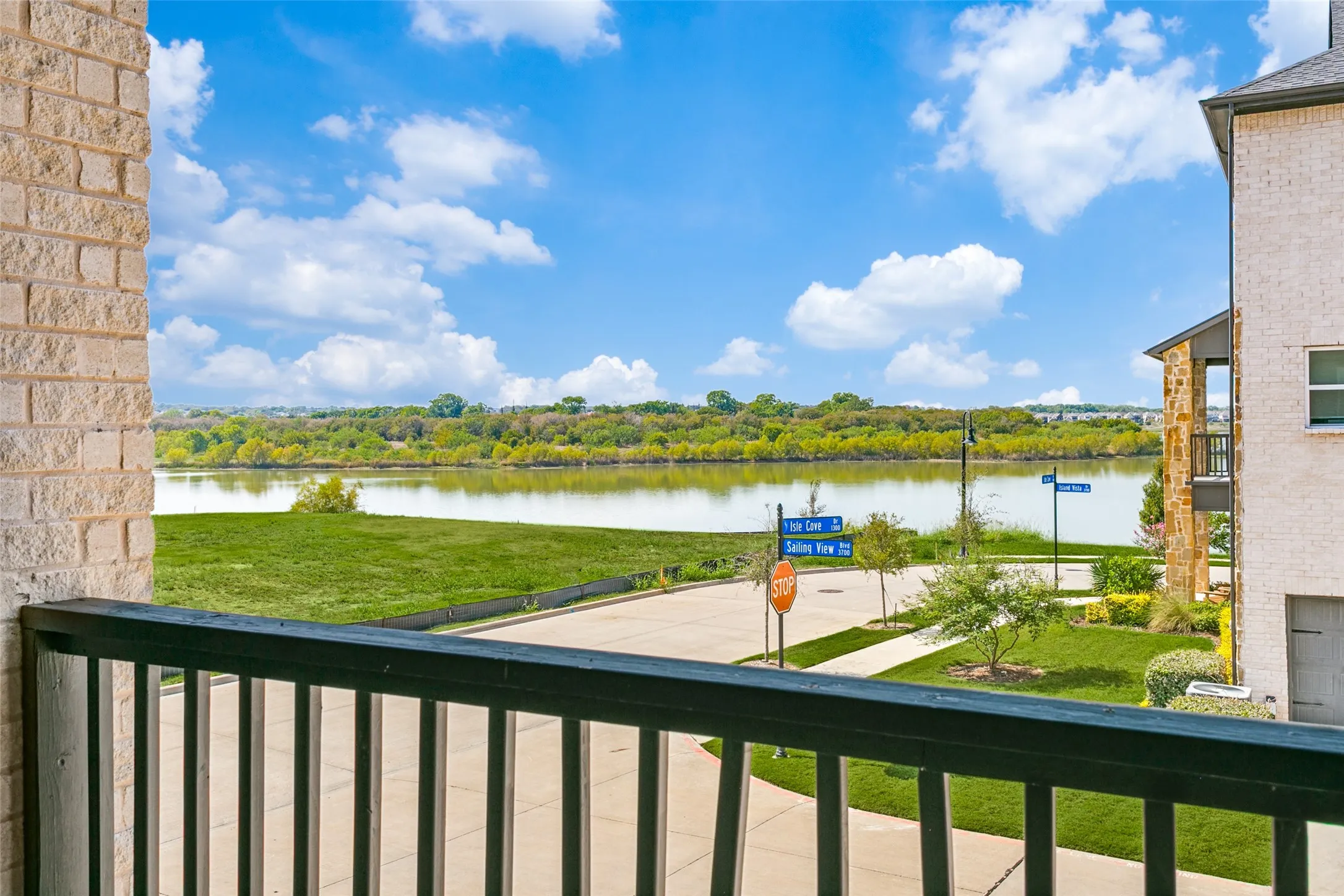 Waterfront setting with expansive green space, brick exterior, and a private balcony with metal railings