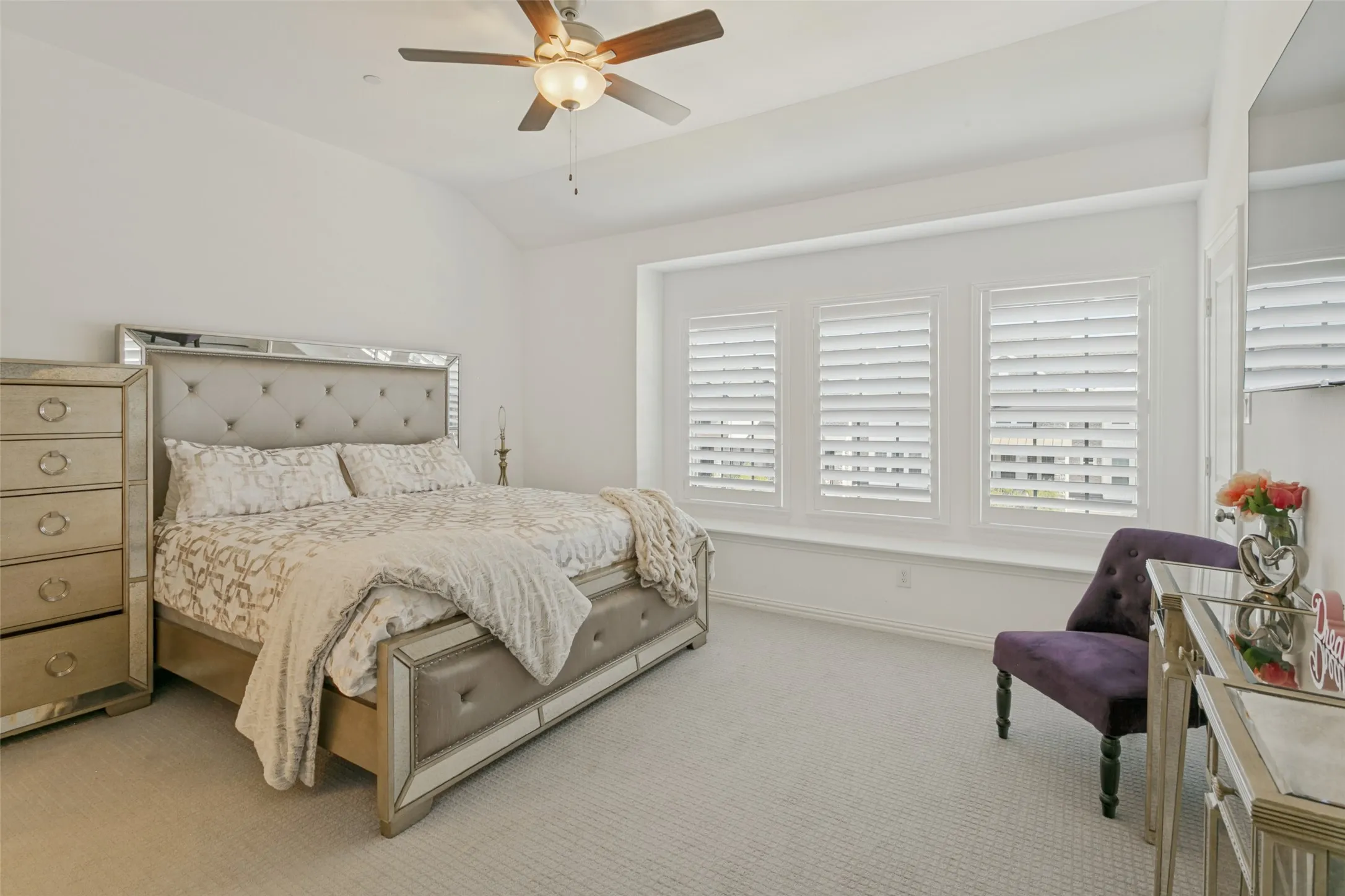 Vaulted ceiling with a ceiling fan, three windows with plantation shutters, light-colored carpeting, and neutral wall tones